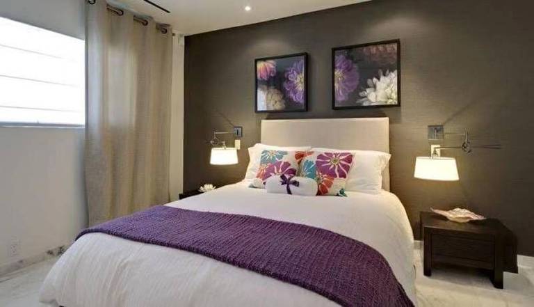 This Toronto interior design project features a contemporary bedroom highlighted by a bold accent wall, symmetrical bedside lighting, and carefully curated soft furnishings. The dark feature wall adds depth and contrast, while the neutral bedding and textured purple throw introduce warmth and personality. Integrated wall-mounted lighting enhances ambiance without cluttering the space, reflecting thoughtful space planning and modern design principles. Completed by Reno Compass Inc., this bedroom renovation delivers comfort, balance, and refined interior styling.