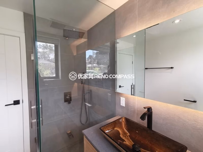 Modern bathroom completed as part of a North York interior renovation, featuring a frameless glass shower enclosure, large-format wall tiles, and a custom vanity with vessel sink. The walk-in shower includes a ceiling-mounted rain shower and minimalist fixtures, creating a clean and open spatial feel. Integrated mirror lighting and natural daylight enhance brightness while maintaining a refined, contemporary aesthetic. Designed and built by a Toronto renovation company with attention to layout efficiency, material selection, and long-term durability.