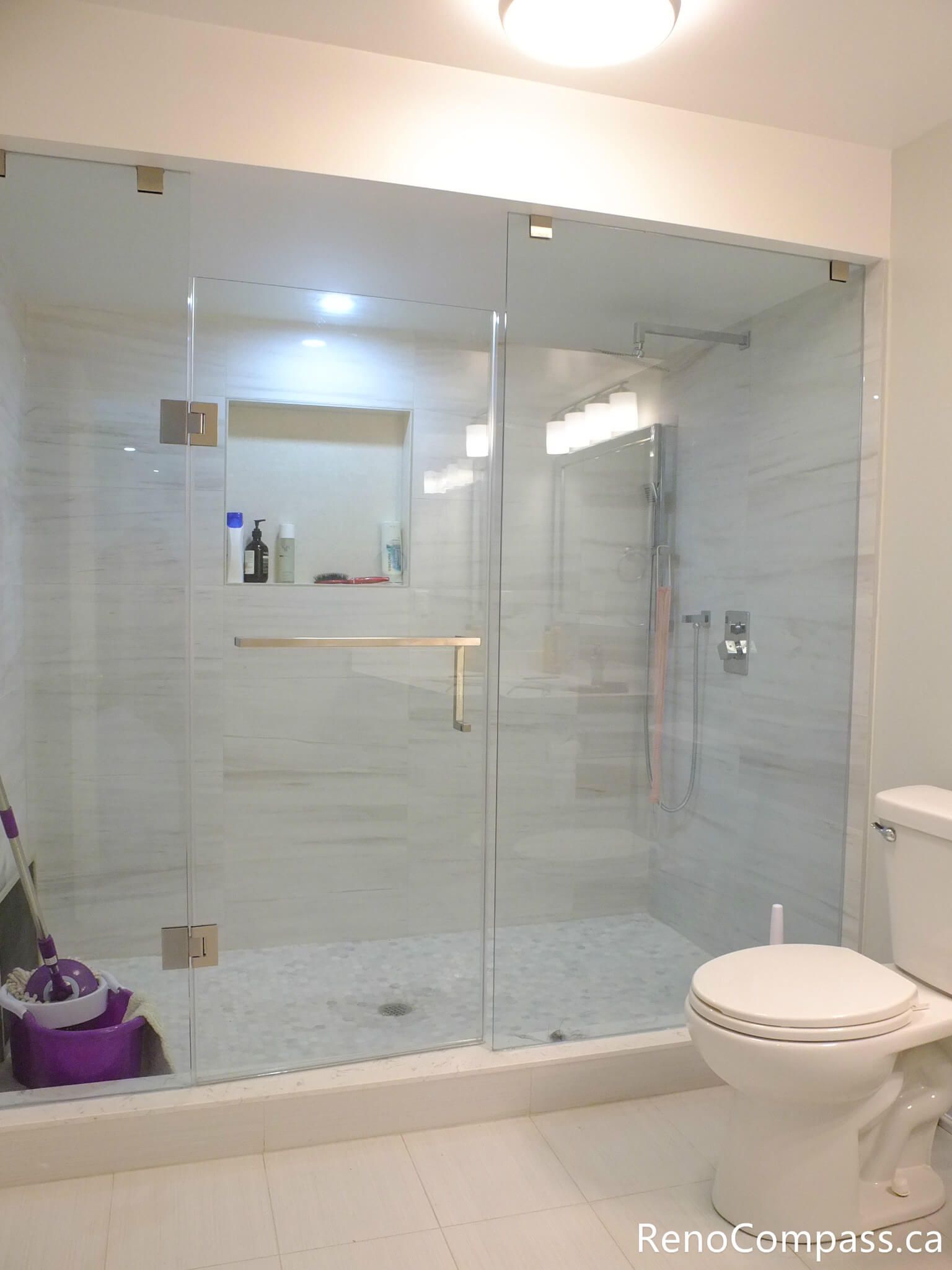 This Markham basement bathroom features a sleek frameless glass walk-in shower with large-format wall tiles and a built-in niche for convenient storage. The clean layout, modern fixtures, and bright finishes create a functional and low-maintenance bathroom space, perfect for basement living or rental units. Completed by a trusted Toronto Renovation Company, Reno Compass Inc.