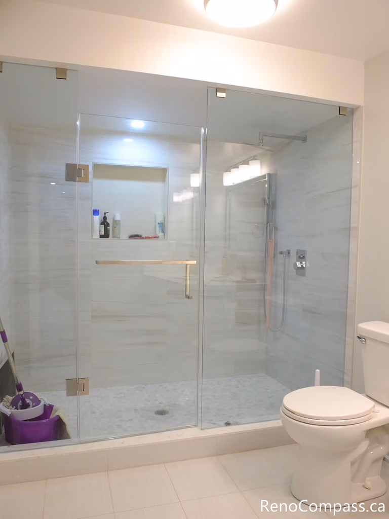 This Markham basement bathroom features a sleek frameless glass walk-in shower with large-format wall tiles and a built-in niche for convenient storage. The clean layout, modern fixtures, and bright finishes create a functional and low-maintenance bathroom space, perfect for basement living or rental units. Completed by a trusted Toronto Renovation Company, Reno Compass Inc.