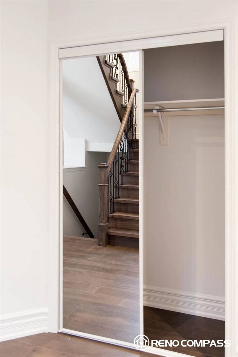 This Markham interior renovation showcases a clean and functional closet design featuring sliding mirrored doors that enhance space and natural light. The updated hardwood flooring seamlessly connects to a beautifully crafted staircase with dark wood finishes and iron balusters, creating a modern and cohesive look for the home.