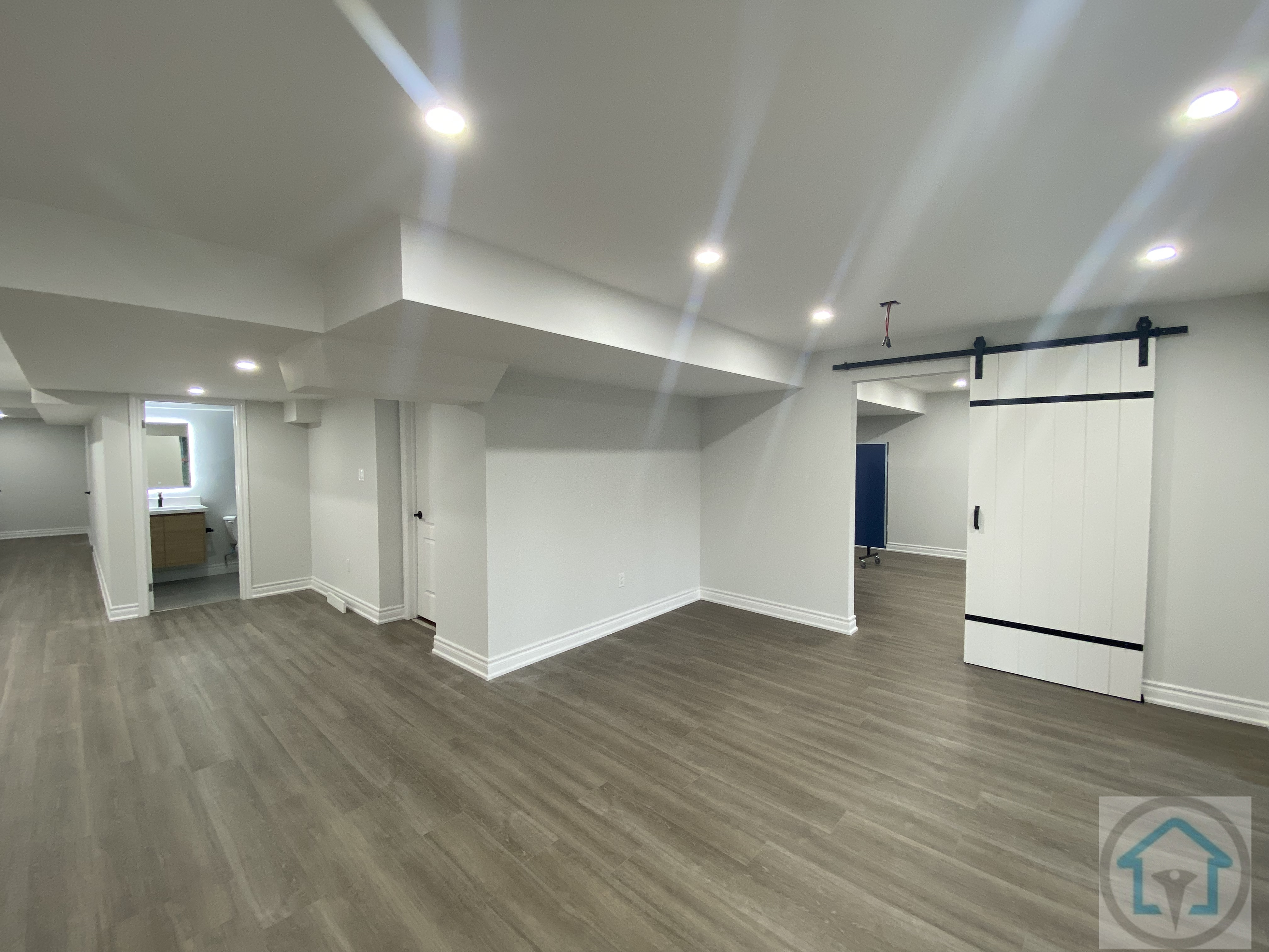 This Aurora basement renovation features an open-concept layout with modern flooring, bright recessed lighting, and clean white walls. The design maximizes natural light and creates a versatile living space suitable for family activities or entertainment. Contractor: Reno Compass Inc., City: Aurora.
