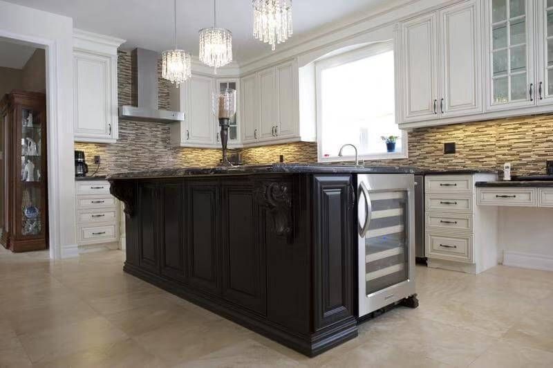This European-style kitchen remodel features a striking dark wood island with decorative panel detailing, creating a strong visual centerpiece within the space. The island is paired with a built-in wine cooler and topped with a polished natural stone countertop for both durability and elegance.

Surrounding white custom cabinetry with classic molding enhances brightness and balance, while the stacked stone backsplash and stainless steel range hood add texture and depth. Crystal pendant lighting above the island elevates the overall sophistication of the kitchen.

Designed for both functionality and luxury, this kitchen renovation combines traditional European craftsmanship with modern convenience, making it ideal for homeowners seeking a timeless and upscale kitchen transformation.