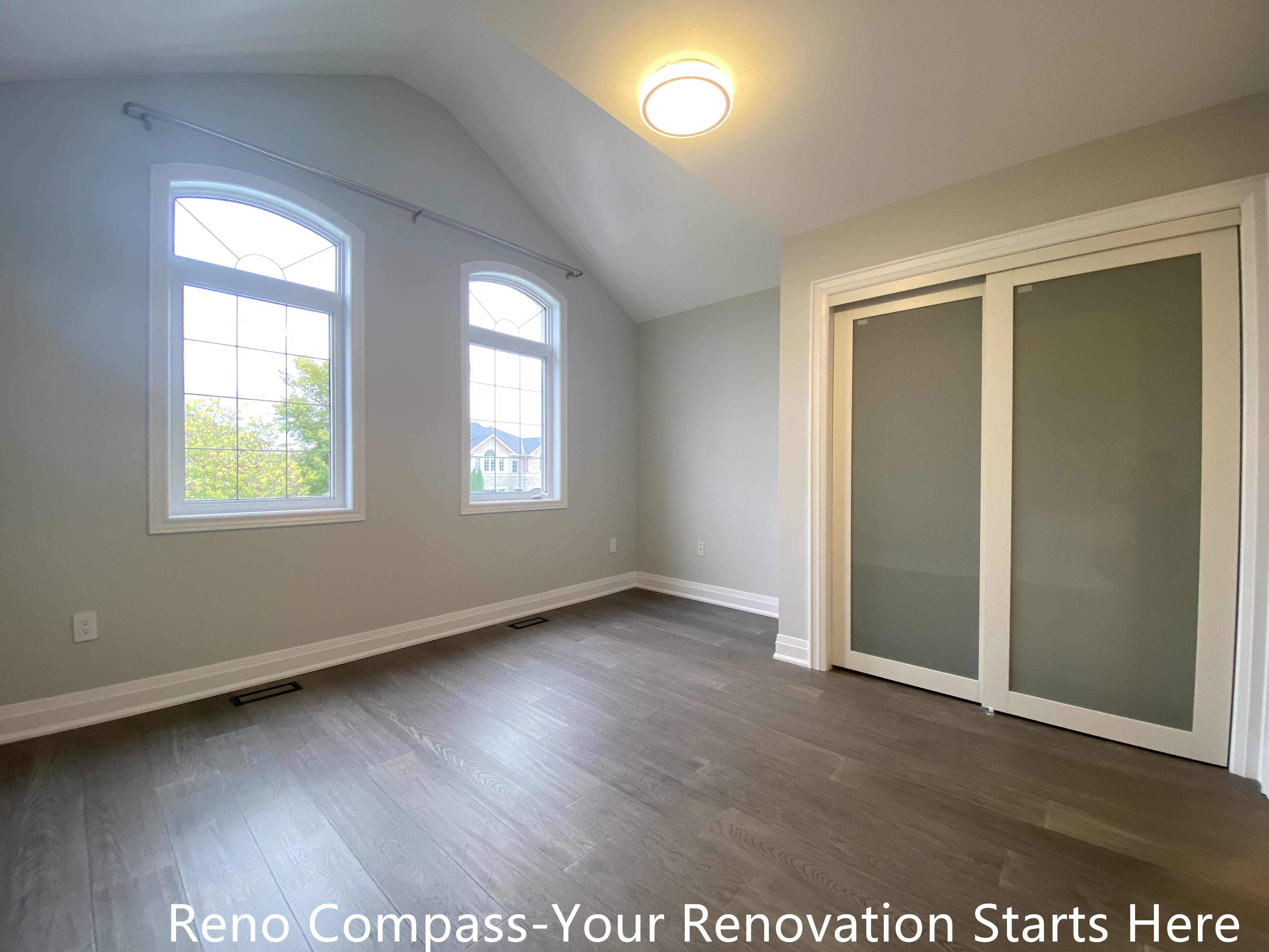 Bright and modern interior renovation in Oakville featuring a bedroom with vaulted ceiling, large arched windows, sliding closet doors, neutral wall colors, and engineered hardwood flooring. This Oakville interior renovation highlights clean finishes, natural light, and functional layout designed by a professional Toronto renovation company.