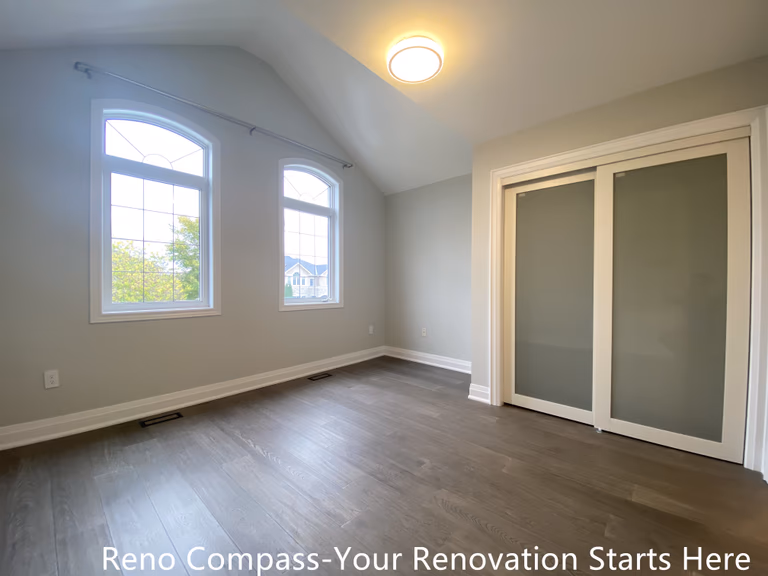 Bright and modern interior renovation in Oakville featuring a bedroom with vaulted ceiling, large arched windows, sliding closet doors, neutral wall colors, and engineered hardwood flooring. This Oakville interior renovation highlights clean finishes, natural light, and functional layout designed by a professional Toronto renovation company.