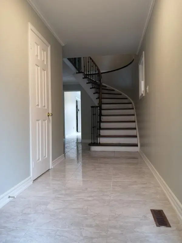 This image showcases a bright and refined hallway renovation in Mississauga, featuring polished tile flooring, soft neutral wall colors, and a custom curved staircase with black iron railings. The redesign improves visual flow from the entryway while enhancing natural light and spatial depth. Completed by an experienced Toronto renovation company, this interior renovation focuses on craftsmanship, elegant circulation, and long-term residential value.