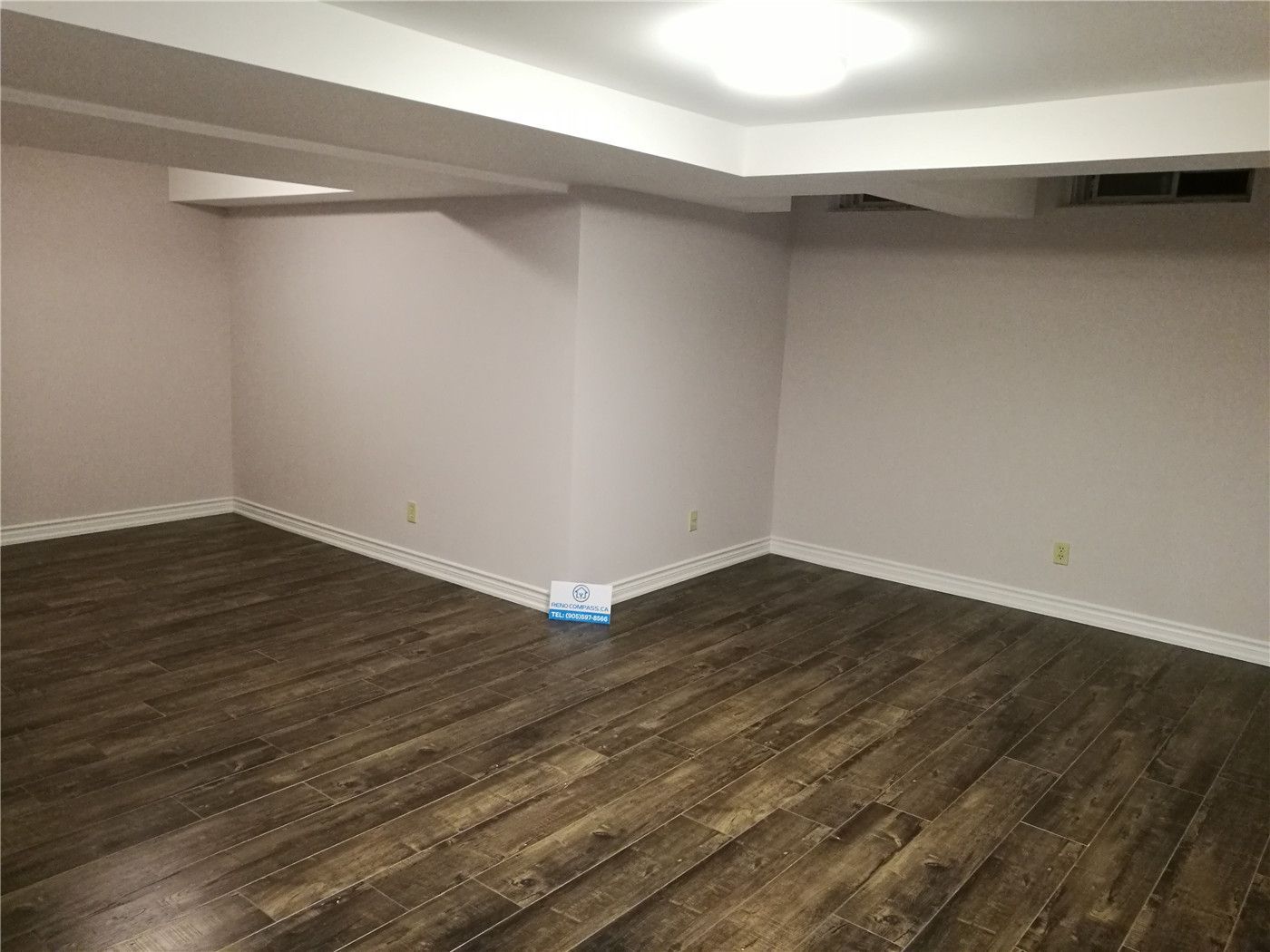 This image shows a completed basement area as part of a Markham basement renovation project. The space features durable vinyl plank flooring, freshly painted neutral walls, and clean white baseboard detailing. The simple rectangular layout allows for flexible use as a family room, home office, storage area, or recreation space. Low-profile ceiling beams are neatly finished to maintain headroom while ensuring structural integrity. This renovation highlights the practical design and quality workmanship delivered by a professional Toronto Renovation Company.