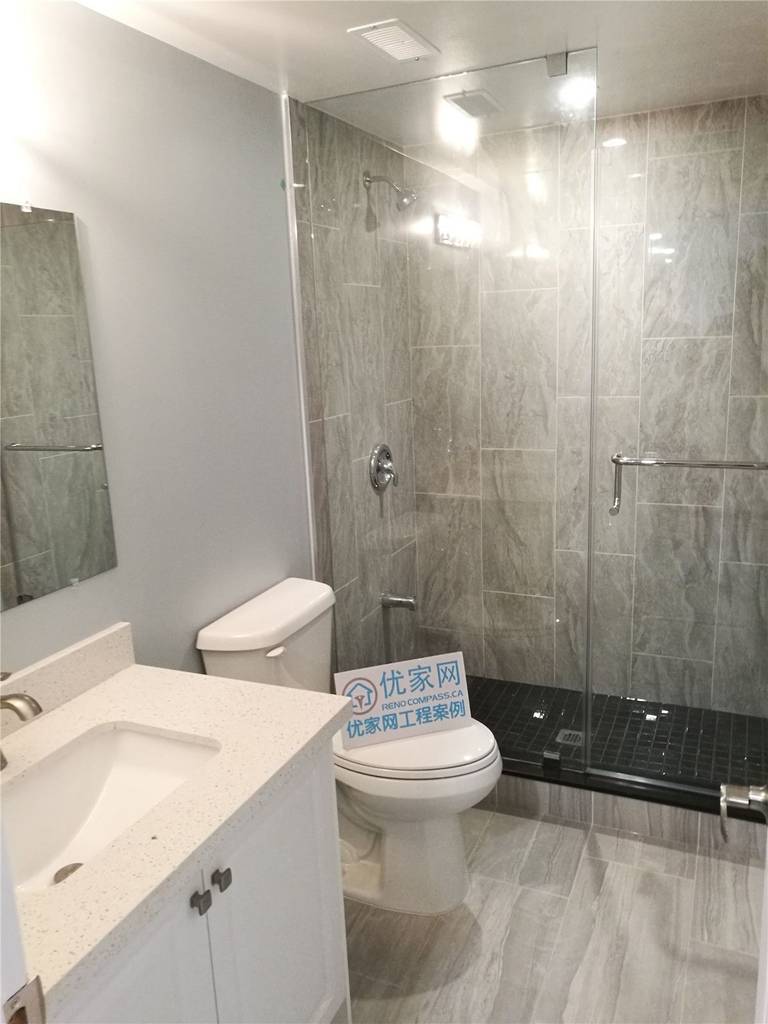 This image showcases a completed basement bathroom as part of a North York interior renovation project. The space features a modern glass-enclosed shower, large-format grey wall tiles, matching floor tiles, and a clean white vanity with an integrated sink. Recessed lighting and a frameless glass shower door enhance brightness and visual openness, while the layout prioritizes functionality and ease of maintenance. This North York interior renovation reflects clean workmanship, durable material selection, and practical bathroom design by a professional Toronto renovation company.