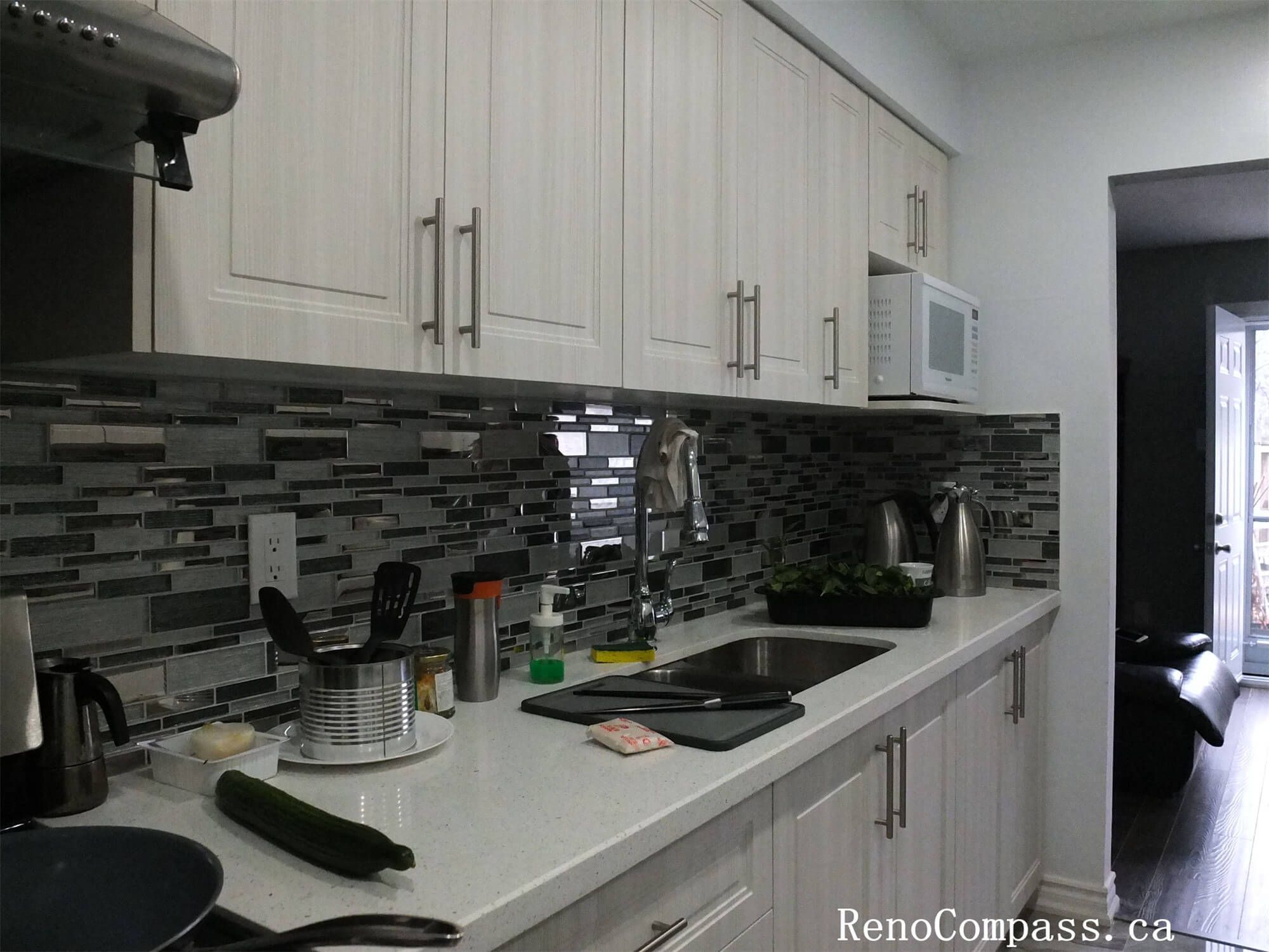 This North York interior renovation features a streamlined galley kitchen with full-height cabinetry, quartz countertop surfaces, and a modern mosaic tile backsplash. The linear layout maximizes storage and workspace efficiency, while integrated lighting and durable finishes create a bright, functional kitchen environment suitable for everyday use in this Toronto home renovation project.