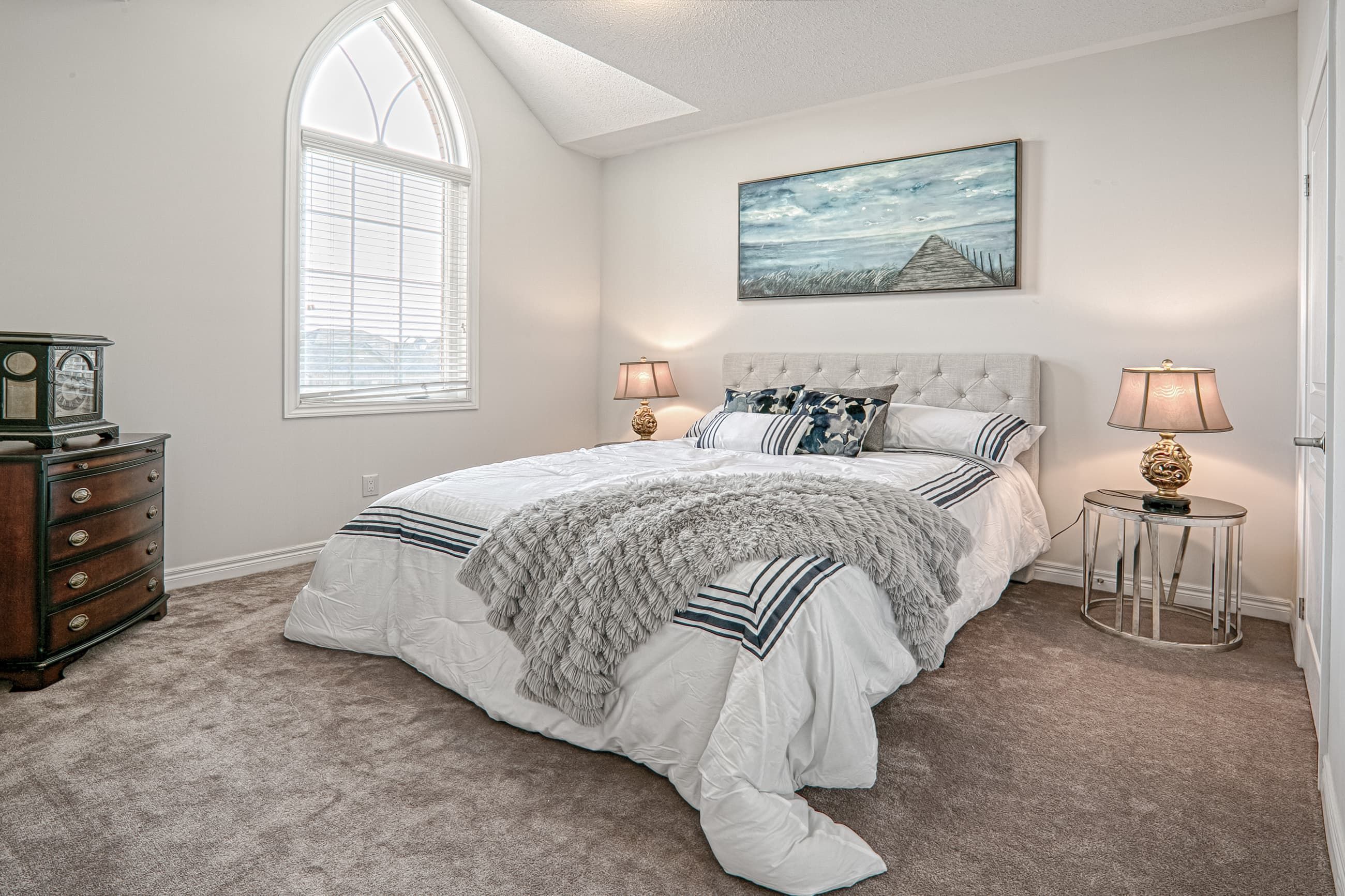 This Toronto luxury bedroom renovation features a bright and elegant master bedroom with high ceilings, a large arched window, and soft neutral finishes that create a calm and comfortable atmosphere. The space includes premium carpeting, modern lighting fixtures, and refined interior styling that enhances both relaxation and functionality. Completed by a professional Toronto renovation company, this residential interior project highlights thoughtful design, quality craftsmanship, and timeless comfort tailored for modern living.