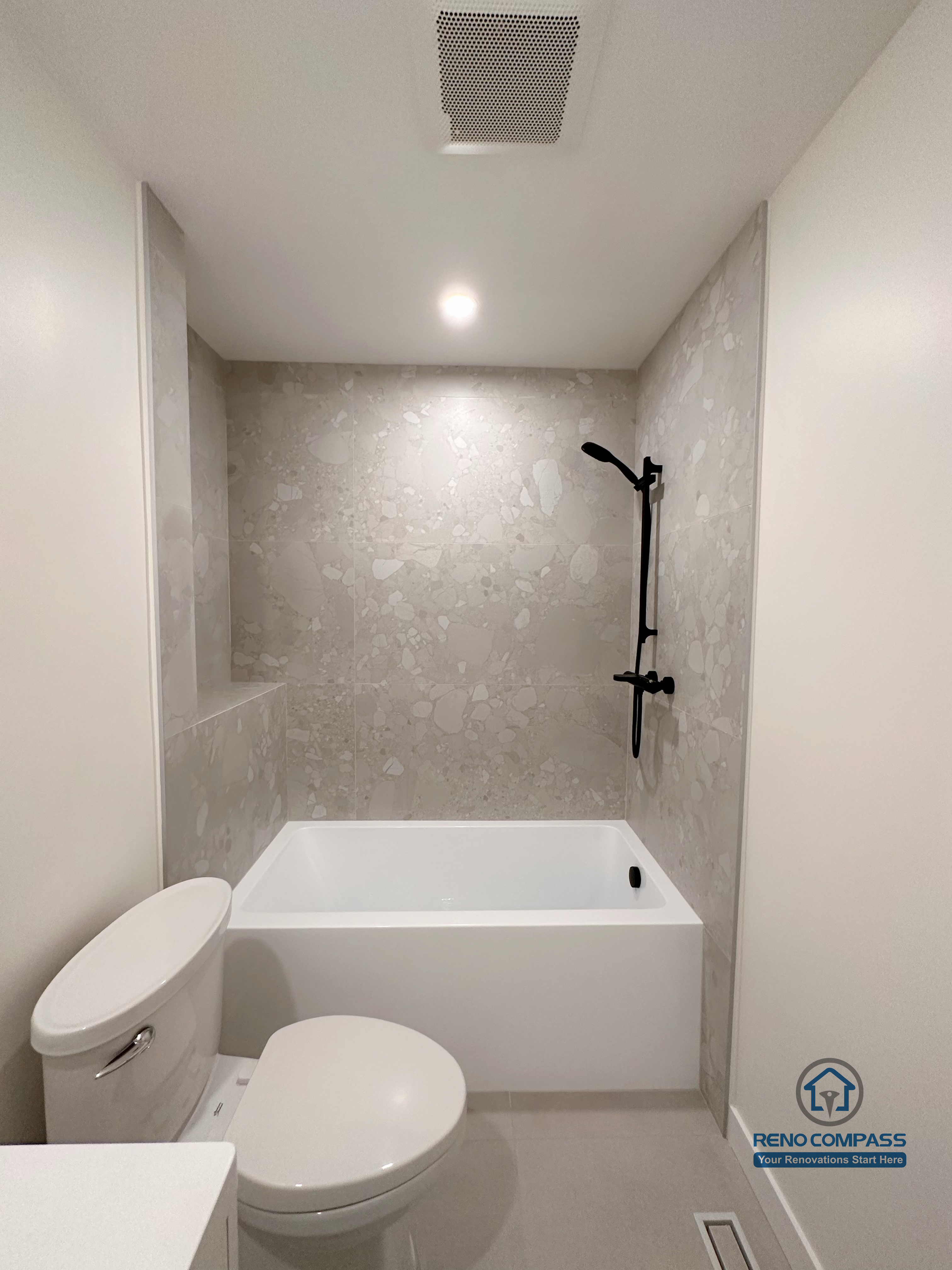 Compact bathroom renovation in Markham featuring a tub and shower combination with large-format wall tiles, matte black shower fixtures, and a clean, minimalist layout. The design maximizes functionality and comfort while maintaining a modern, low-maintenance bathroom environment.