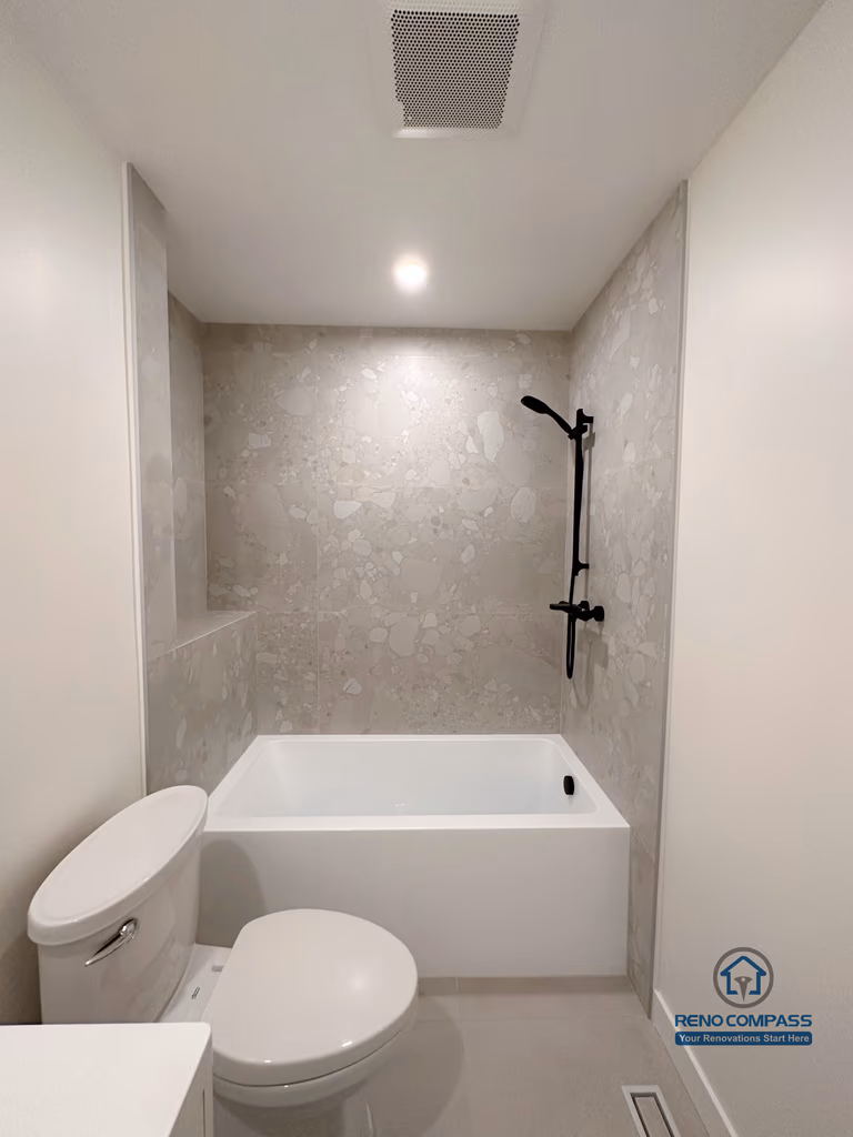 Compact bathroom renovation in Markham featuring a tub and shower combination with large-format wall tiles, matte black shower fixtures, and a clean, minimalist layout. The design maximizes functionality and comfort while maintaining a modern, low-maintenance bathroom environment.