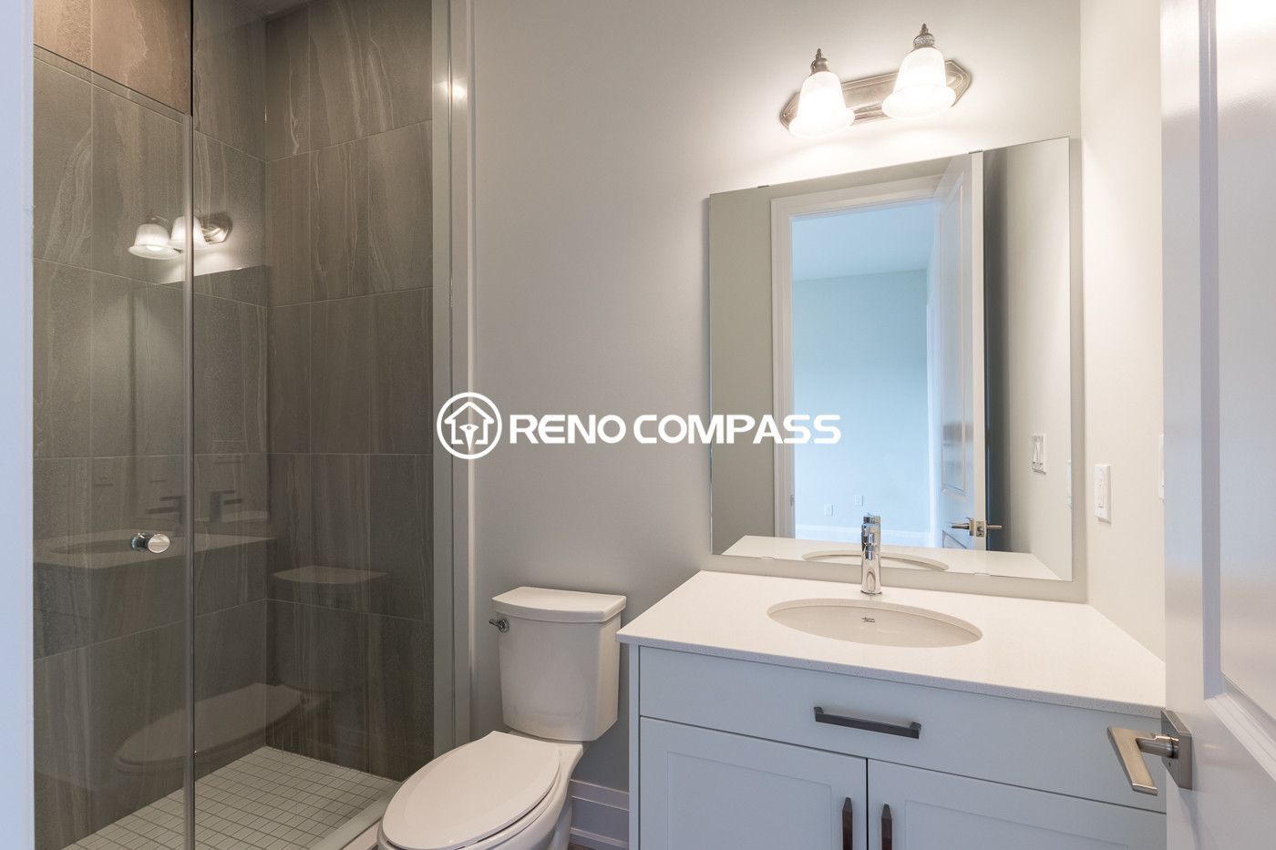 Contemporary bathroom renovation in Newmarket featuring a modern vanity with quartz countertop, large wall mirror, and a frameless glass shower enclosure. Completed by a professional Toronto renovation company, this design creates a bright and practical bathroom space with a clean modern style.