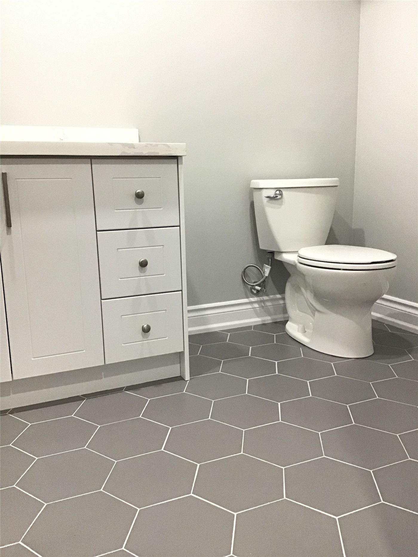 Contemporary basement bathroom renovation in Newmarket featuring grey hexagon floor tiles, white vanity cabinetry, and clean neutral wall finishes. This thoughtfully designed space combines durability, simplicity, and modern style to complete the fully finished basement.