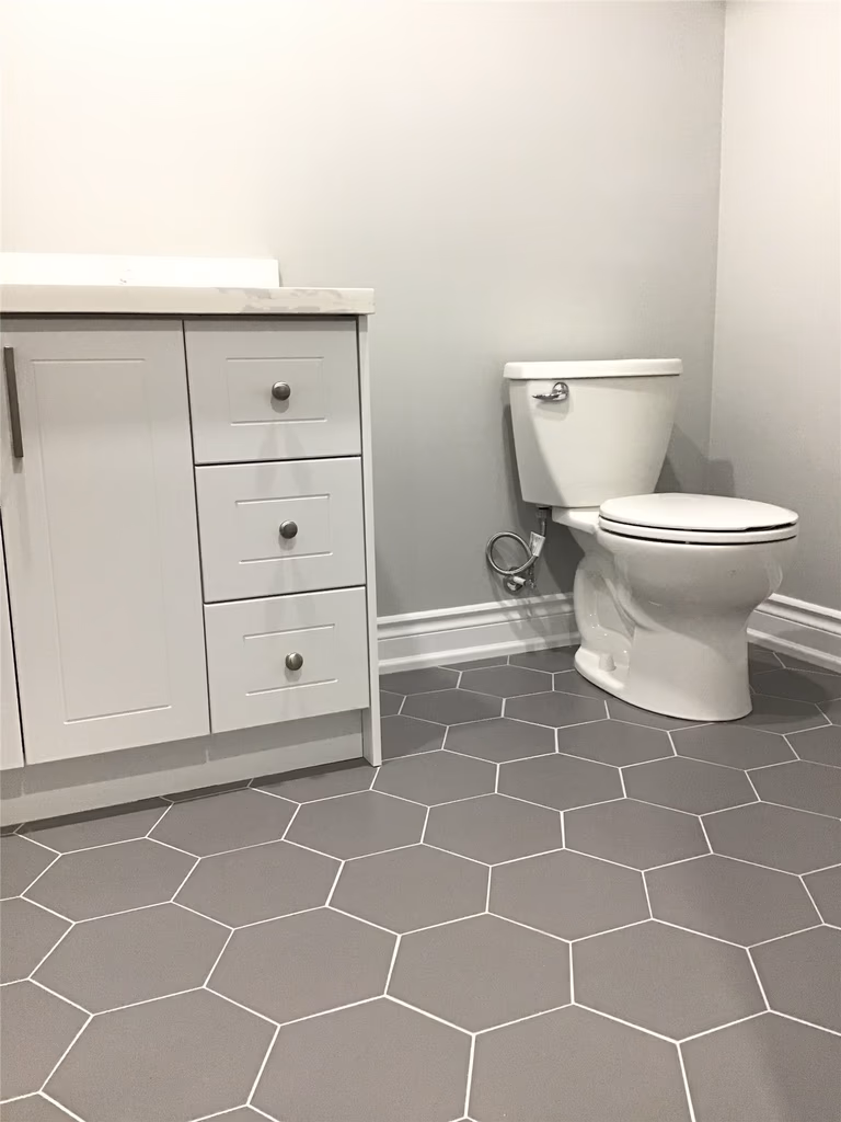 Contemporary basement bathroom renovation in Newmarket featuring grey hexagon floor tiles, white vanity cabinetry, and clean neutral wall finishes. This thoughtfully designed space combines durability, simplicity, and modern style to complete the fully finished basement.