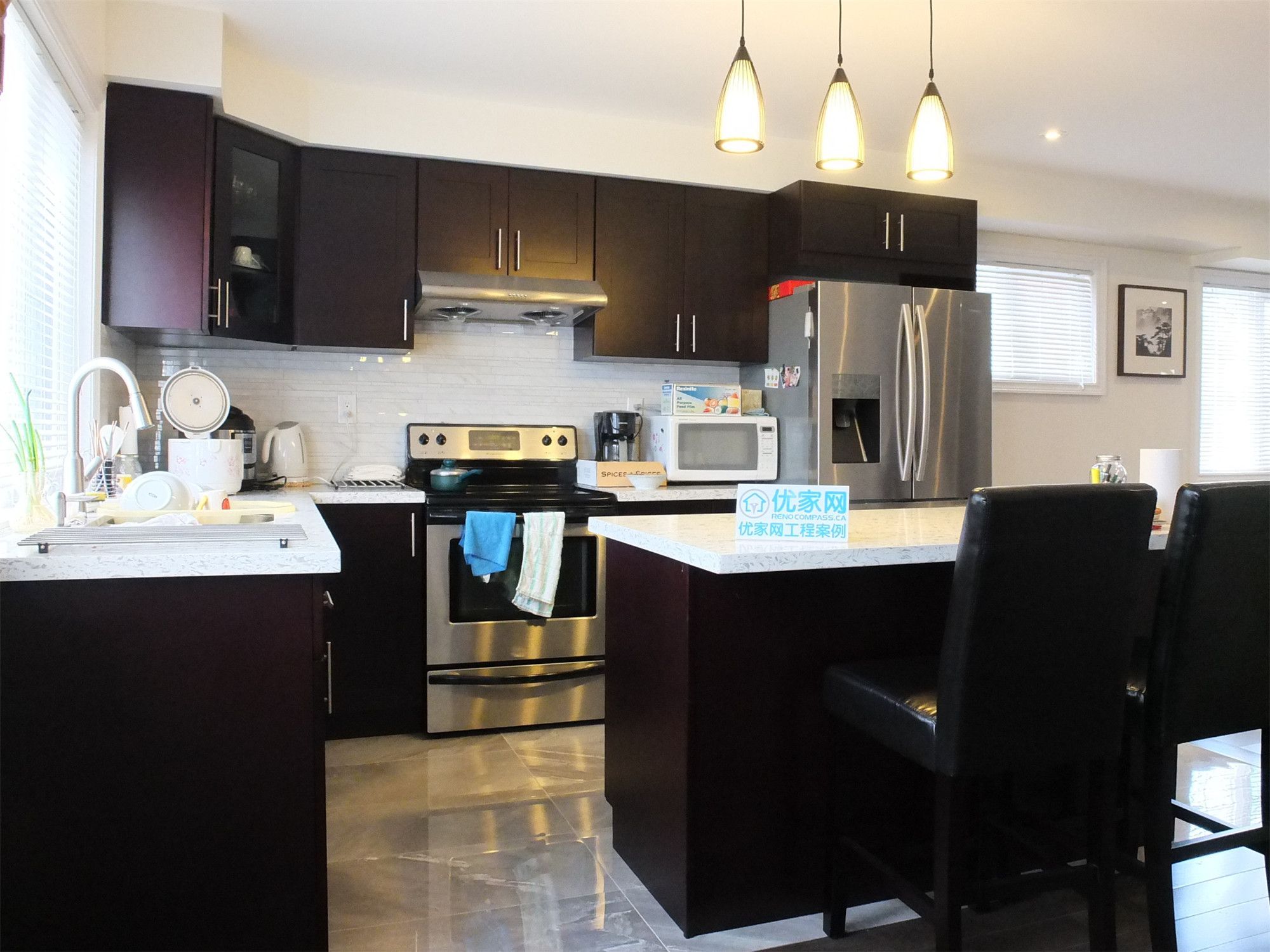 Contemporary kitchen from a Scarborough home addition project featuring dark wood cabinetry, quartz countertops, stainless steel appliances, and a functional kitchen island with pendant lighting. The renovation enhances both cooking efficiency and modern interior aesthetics within the expanded living space.