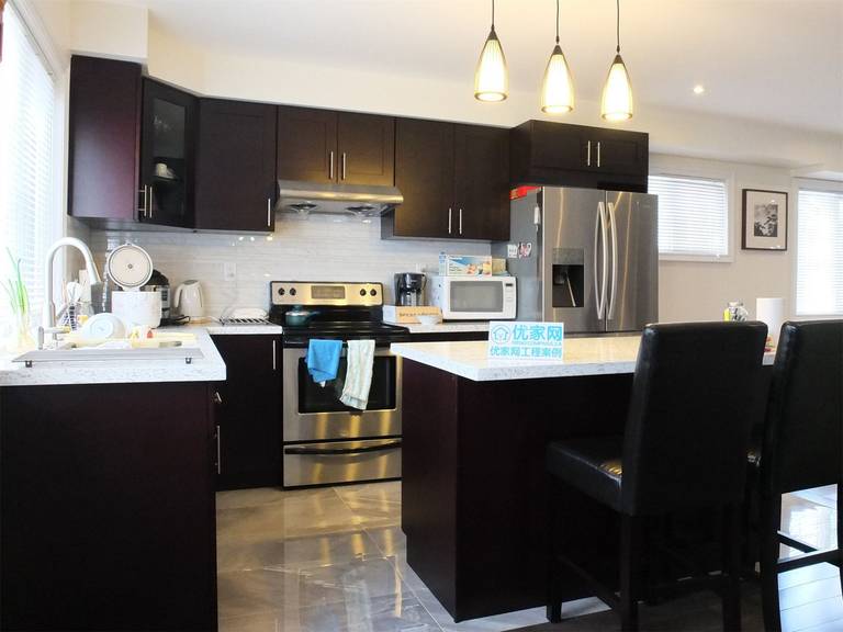 Contemporary kitchen from a Scarborough home addition project featuring dark wood cabinetry, quartz countertops, stainless steel appliances, and a functional kitchen island with pendant lighting. The renovation enhances both cooking efficiency and modern interior aesthetics within the expanded living space.