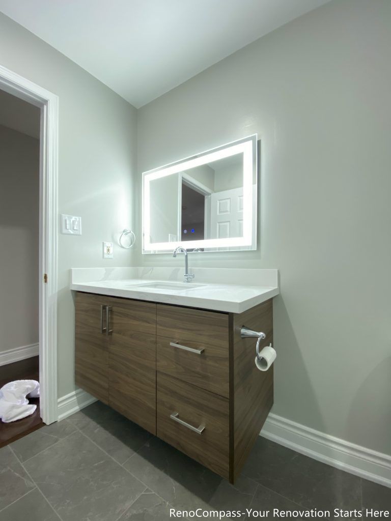 This Oakville bathroom renovation features a modern floating-style vanity with custom wood cabinetry, quartz countertop, and a sleek LED backlit mirror that enhances brightness and functionality. The clean layout is paired with durable floor tiles and contemporary fixtures, creating a simple yet elegant bathroom design. Completed by a trusted Toronto renovation company, this upgrade focuses on maximizing storage, improving lighting, and delivering a modern, practical bathroom space that adds long-term value to the home.