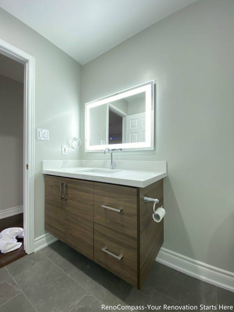 This Oakville bathroom renovation features a modern floating-style vanity with custom wood cabinetry, quartz countertop, and a sleek LED backlit mirror that enhances brightness and functionality. The clean layout is paired with durable floor tiles and contemporary fixtures, creating a simple yet elegant bathroom design. Completed by a trusted Toronto renovation company, this upgrade focuses on maximizing storage, improving lighting, and delivering a modern, practical bathroom space that adds long-term value to the home.