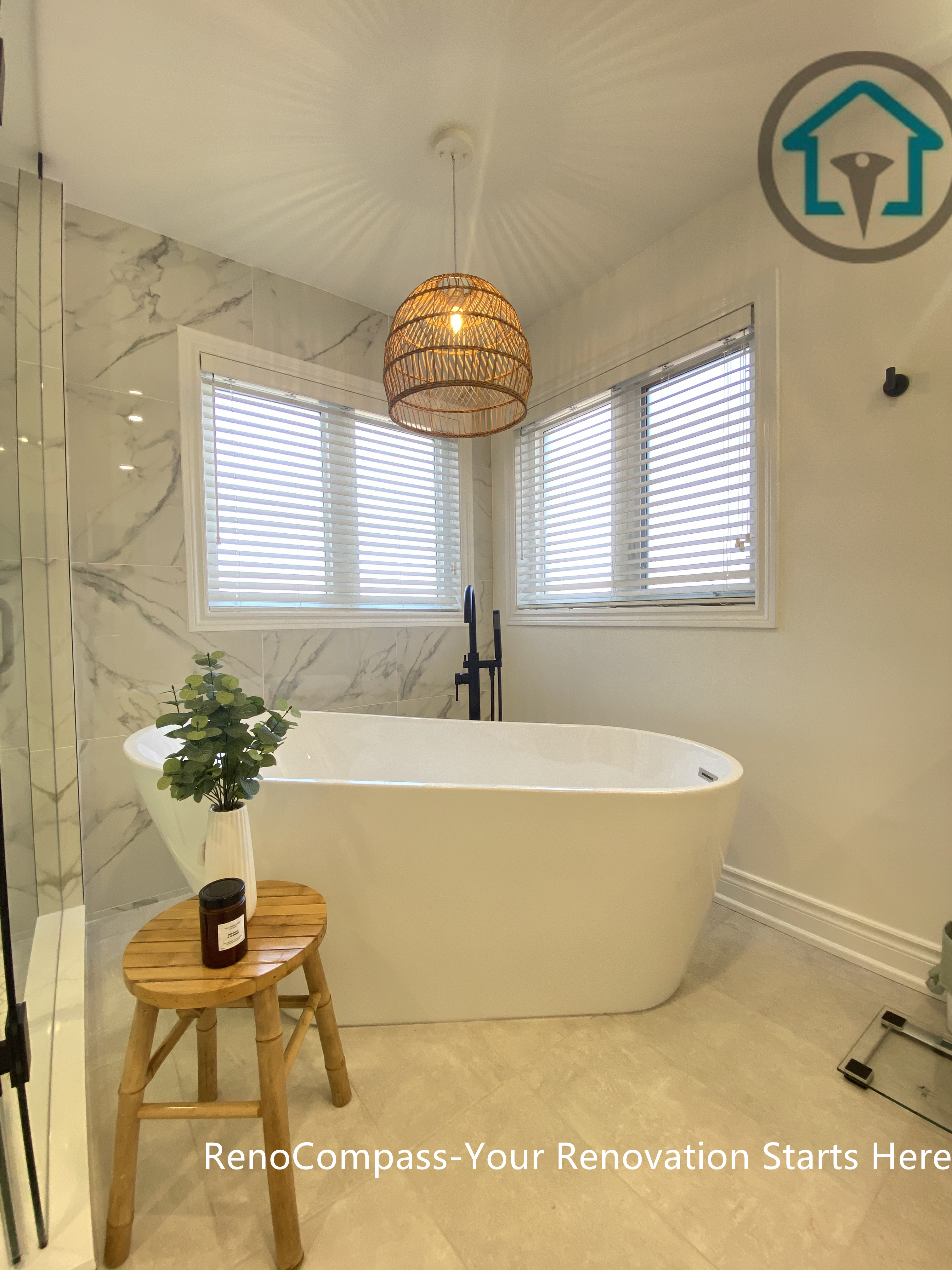Elegant Oakville bathroom renovation featuring a freestanding bathtub positioned by corner windows, complemented by marble-look wall tiles, matte black fixtures, and a warm woven pendant light. This bathroom remodel blends natural light, soft textures, and spa-inspired comfort, completed by a trusted Toronto renovation company.