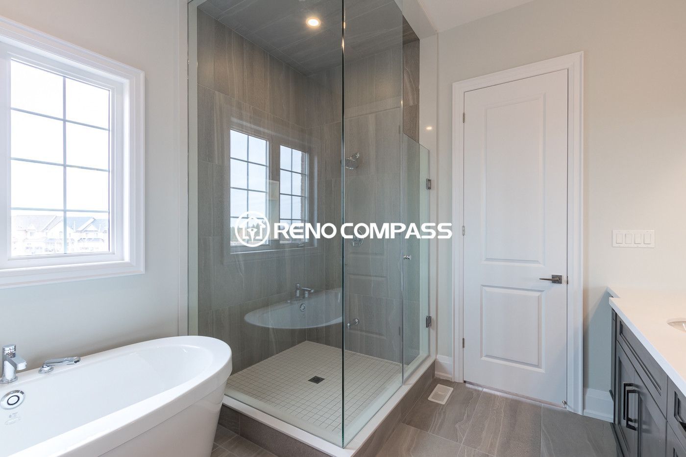 Contemporary bathroom renovation in Newmarket featuring a frameless glass shower enclosure, freestanding bathtub, and modern tile flooring. This elegant layout was completed by a professional Toronto renovation company, creating a bright, spacious and comfortable bathroom environment.