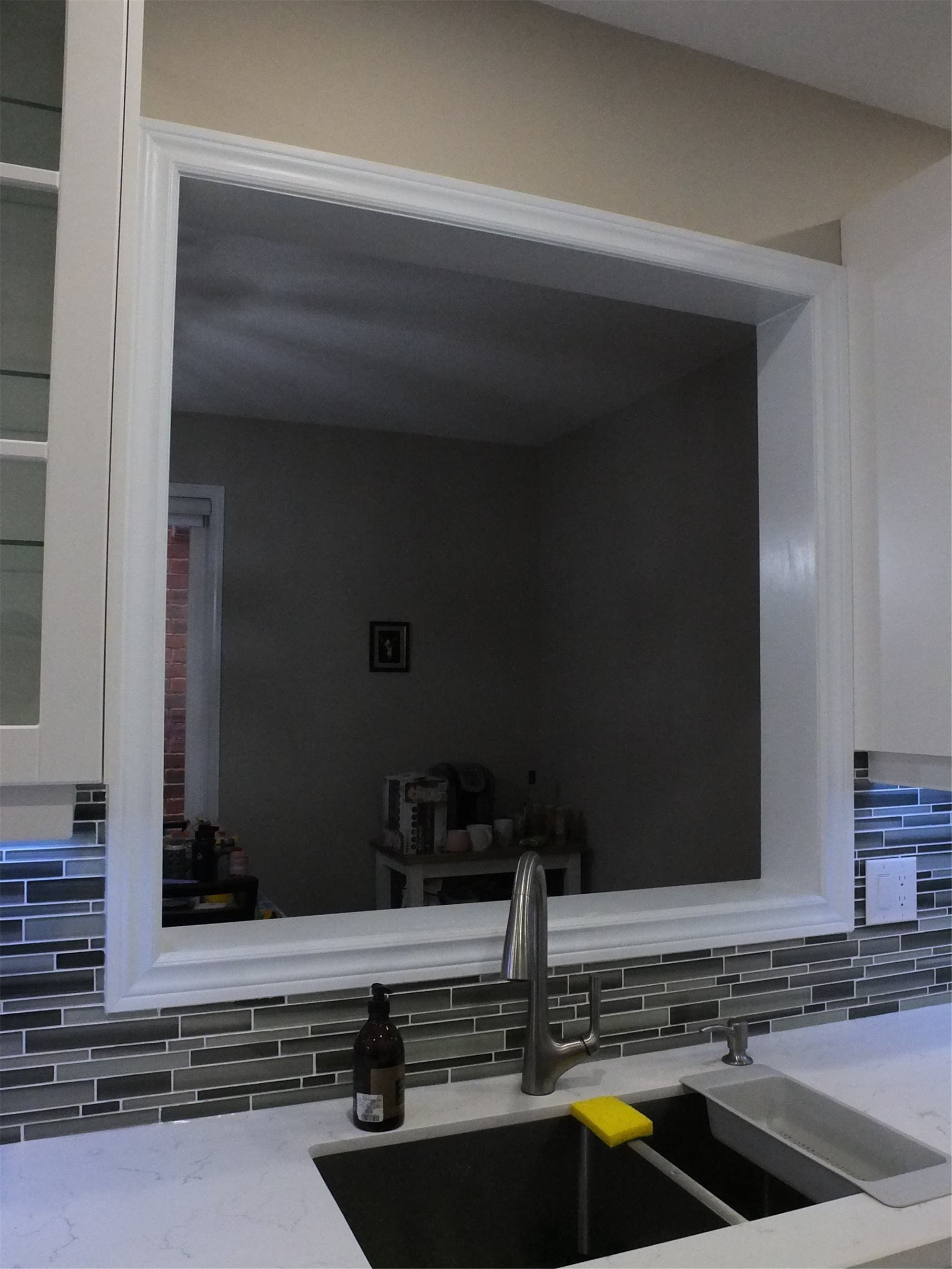 This Vaughan kitchen renovation features a clean pass-through window design above the sink, paired with quartz countertops, white shaker cabinetry, and a modern glass mosaic backsplash. The opening connects the kitchen with the adjacent living space, improving light flow and functionality. Completed by a professional Toronto renovation company, the design combines practical layout improvements with a contemporary aesthetic.
