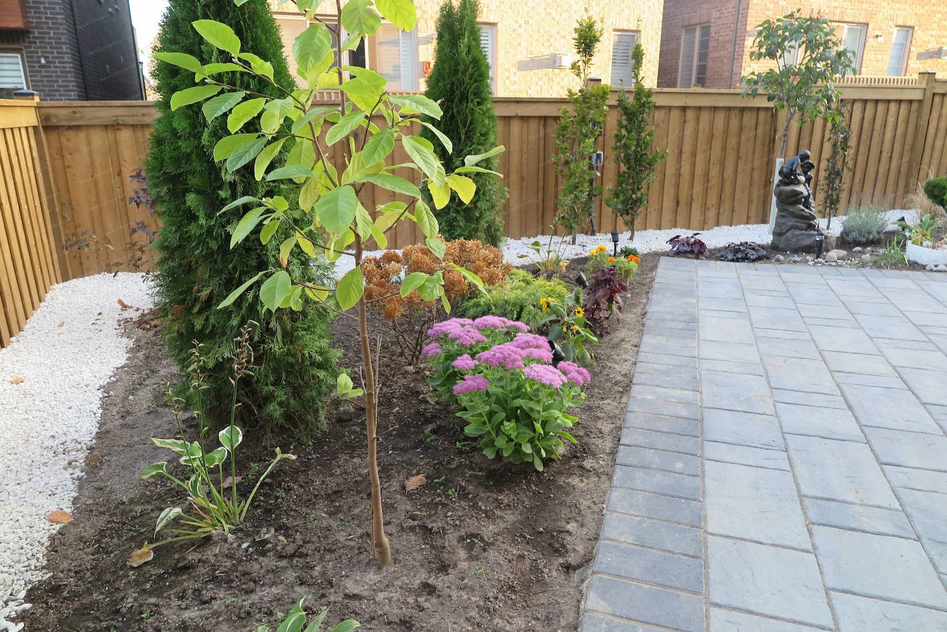 This Vaughan landscaping renovation showcases a clean interlock patio layout alongside a beautifully arranged garden bed with ornamental shrubs, flowering plants, and decorative river rock borders. The design adds color, structure, and a relaxing natural atmosphere to the backyard living space. Expertly completed by Reno Compass Inc
