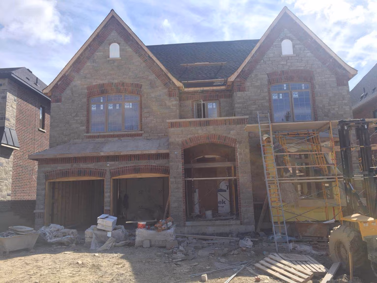 Luxury custom home exterior during the construction phase of a Toronto design build custom build project. The structure features a classic stone and brick façade, arched entryway, large windows, and a double garage layout typical of high-end residential architecture. This project is part of a whole house renovation Toronto and custom build development, showcasing detailed craftsmanship and architectural planning used to create modern luxury homes across Toronto.