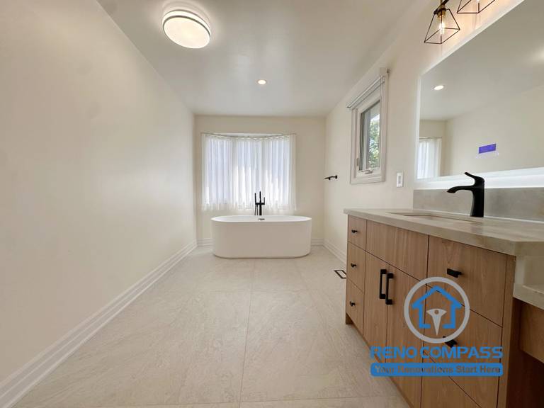 A luxury primary bathroom featuring a freestanding soaking bathtub, custom double vanity, quartz countertops, matte black fixtures, and large-format porcelain tile flooring. Completed during a whole home renovation in Markham, Ontario, this spa-inspired bathroom combines modern elegance, comfort, and premium craftsmanship by Reno Compass.