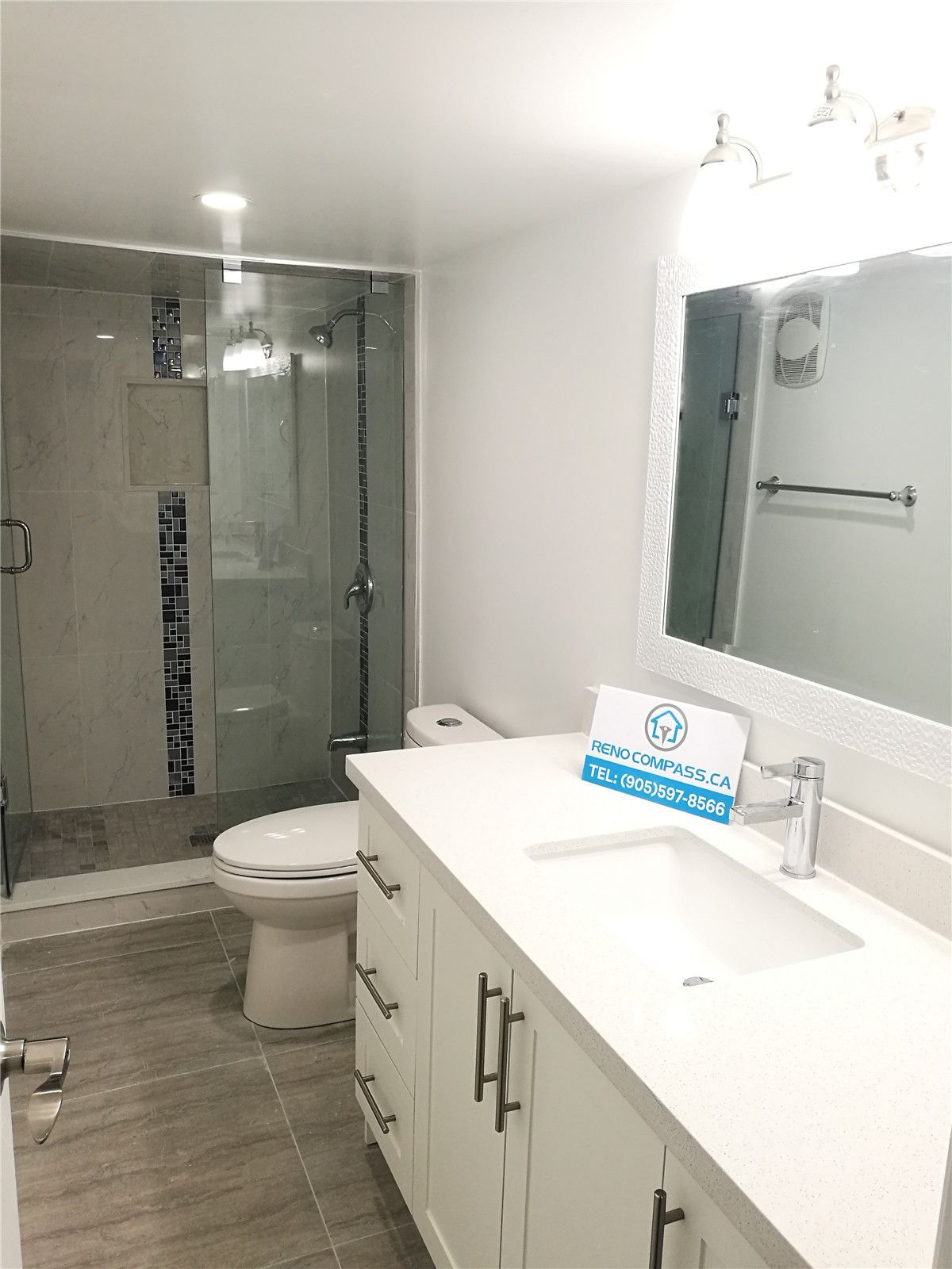 Bathroom renovation project in Pickering featuring a modern white vanity with quartz countertop, undermount sink, large mirror, and a frameless glass shower enclosure. The neutral tile flooring and clean layout enhance brightness and functionality, completed by a professional Toronto renovation company.