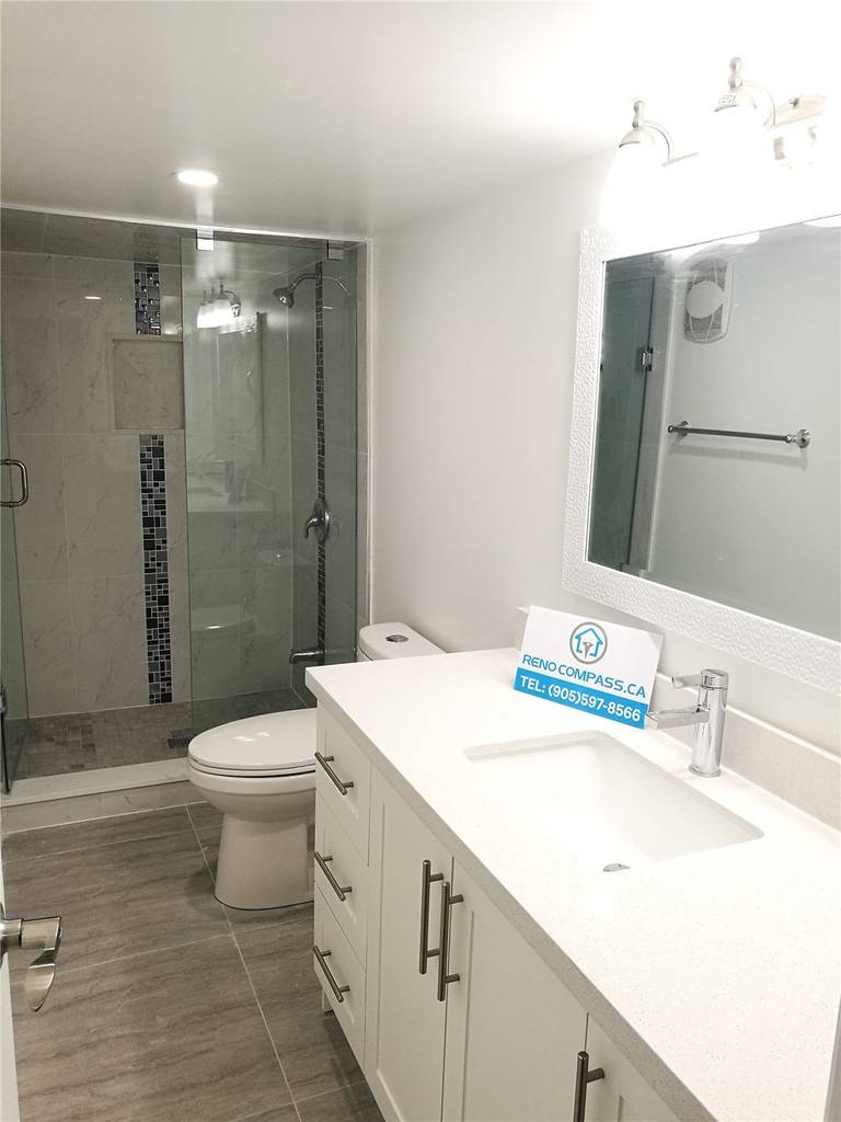 Bathroom renovation project in Pickering featuring a modern white vanity with quartz countertop, undermount sink, large mirror, and a frameless glass shower enclosure. The neutral tile flooring and clean layout enhance brightness and functionality, completed by a professional Toronto renovation company.