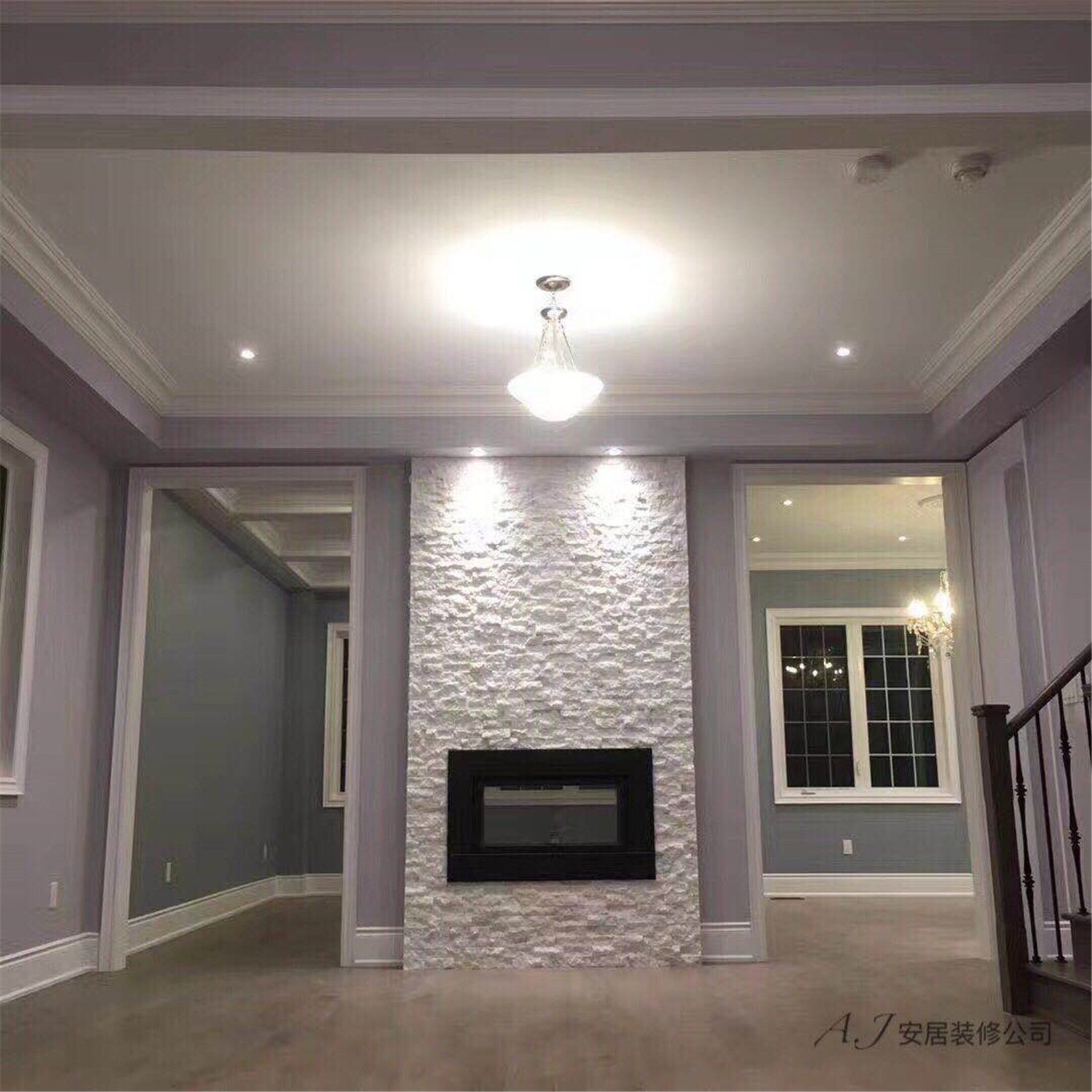 This Scarborough interior renovation showcases a modern living room centered around a textured stone fireplace feature wall. The space is enhanced with elegant crown molding, recessed ceiling lights, and neutral grey wall tones that create a calm and refined atmosphere. Large windows bring in natural light while the warm wood flooring adds balance and warmth to the overall design, highlighting a clean and contemporary interior renovation in Scarborough.