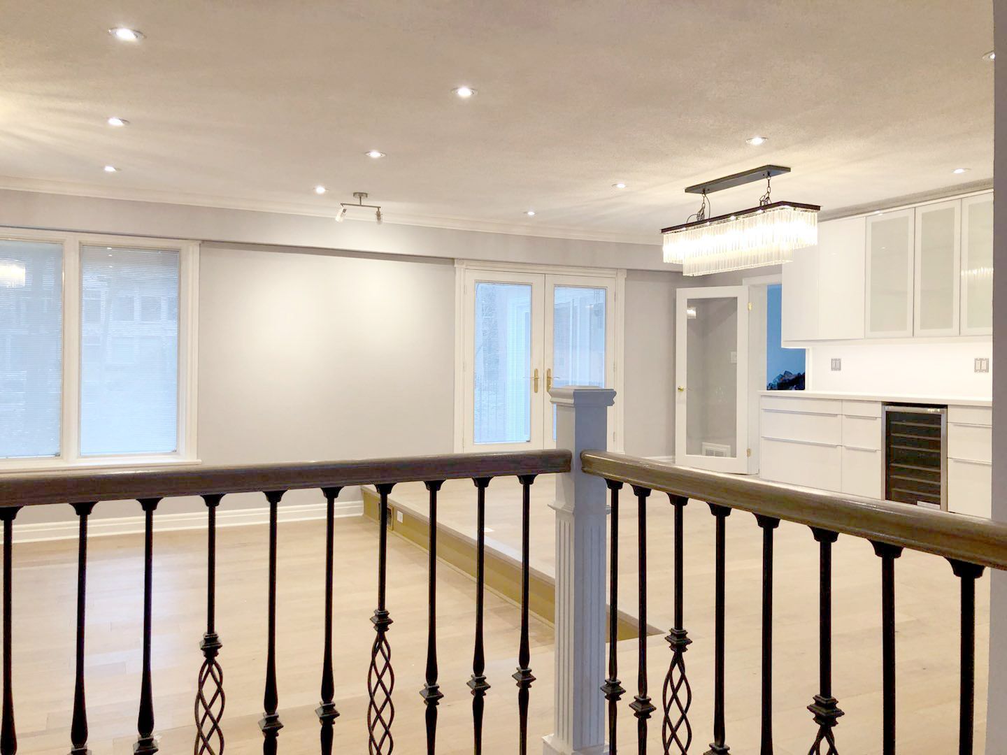This Etobicoke interior renovation showcases a bright open-concept upper level featuring upgraded flooring, recessed lighting, and custom-built cabinetry with integrated wine cooler. Large windows and glass doors enhance natural light, creating an airy and spacious atmosphere. The modern chandelier adds a refined focal point while maintaining a clean and balanced design. Completed by Reno Compass Inc., this renovation improves layout flow, visual openness, and everyday functionality with timeless finishes suitable for contemporary living.