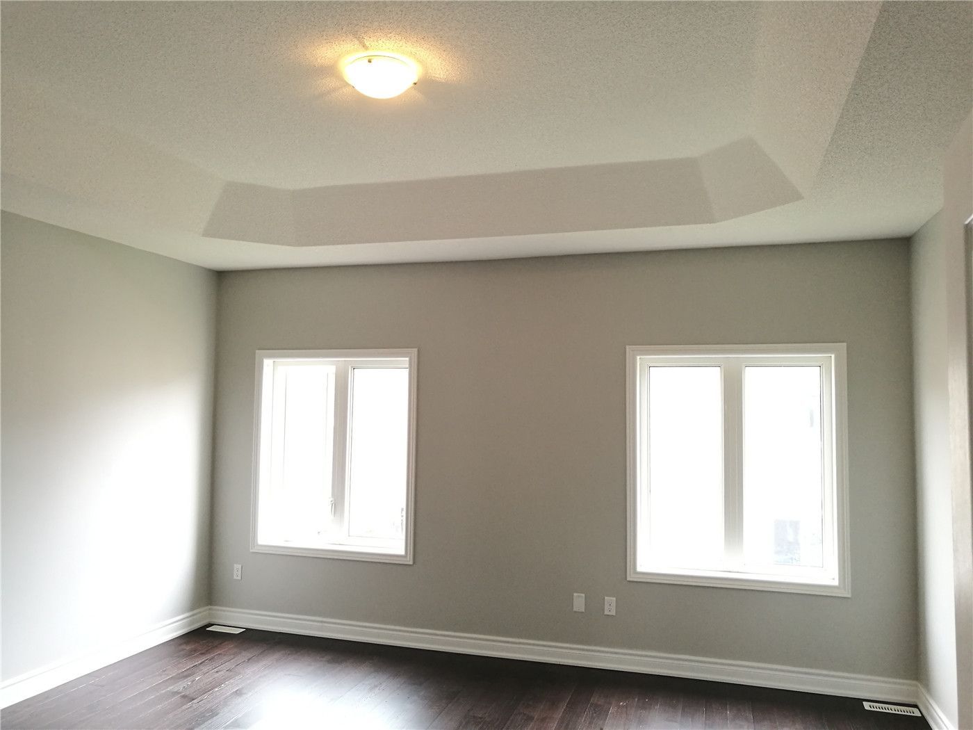 This image shows a bedroom after a Markham interior renovation, featuring a tray ceiling design, soft neutral wall colors, large windows for natural light, and dark hardwood flooring that creates a calm and balanced living environment.