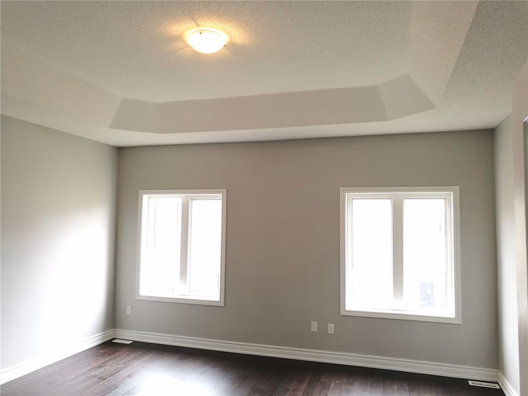 This image shows a bedroom after a Markham interior renovation, featuring a tray ceiling design, soft neutral wall colors, large windows for natural light, and dark hardwood flooring that creates a calm and balanced living environment.