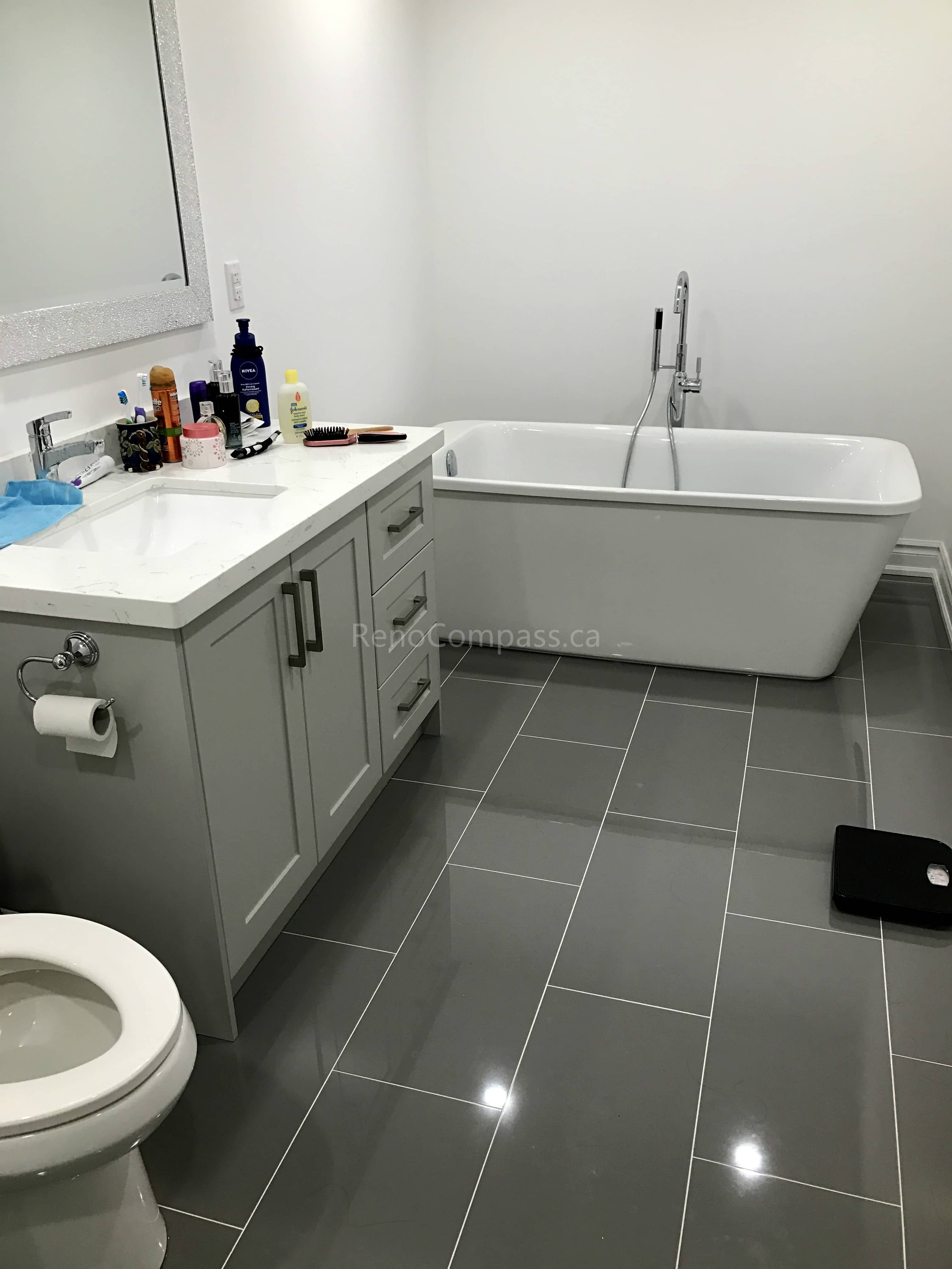 This Toronto bathroom renovation by Reno Compass features a sleek freestanding bathtub paired with a custom vanity and quartz countertop. Large-format grey floor tiles create a clean and contemporary look, while modern fixtures and a spacious layout enhance comfort and functionality. Designed for both relaxation and everyday convenience, this upgraded bathroom combines elegant finishes with durable craftsmanship to increase long-term home value.