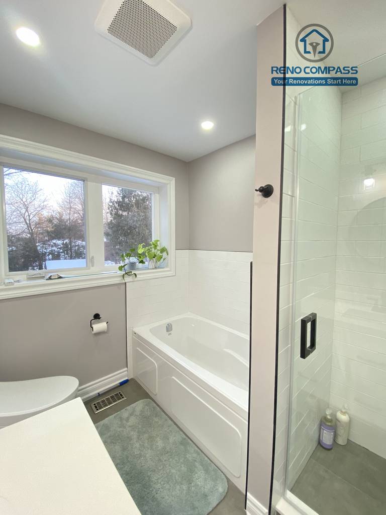 This North York bathroom renovation presents a bright and well-organized layout featuring a built-in bathtub, a glass-enclosed shower, and recessed ceiling lighting. Natural light from the window enhances the soft gray and white color palette, creating a clean and comfortable bathroom space completed by a Toronto renovation company with a focus on practical design and quality execution.