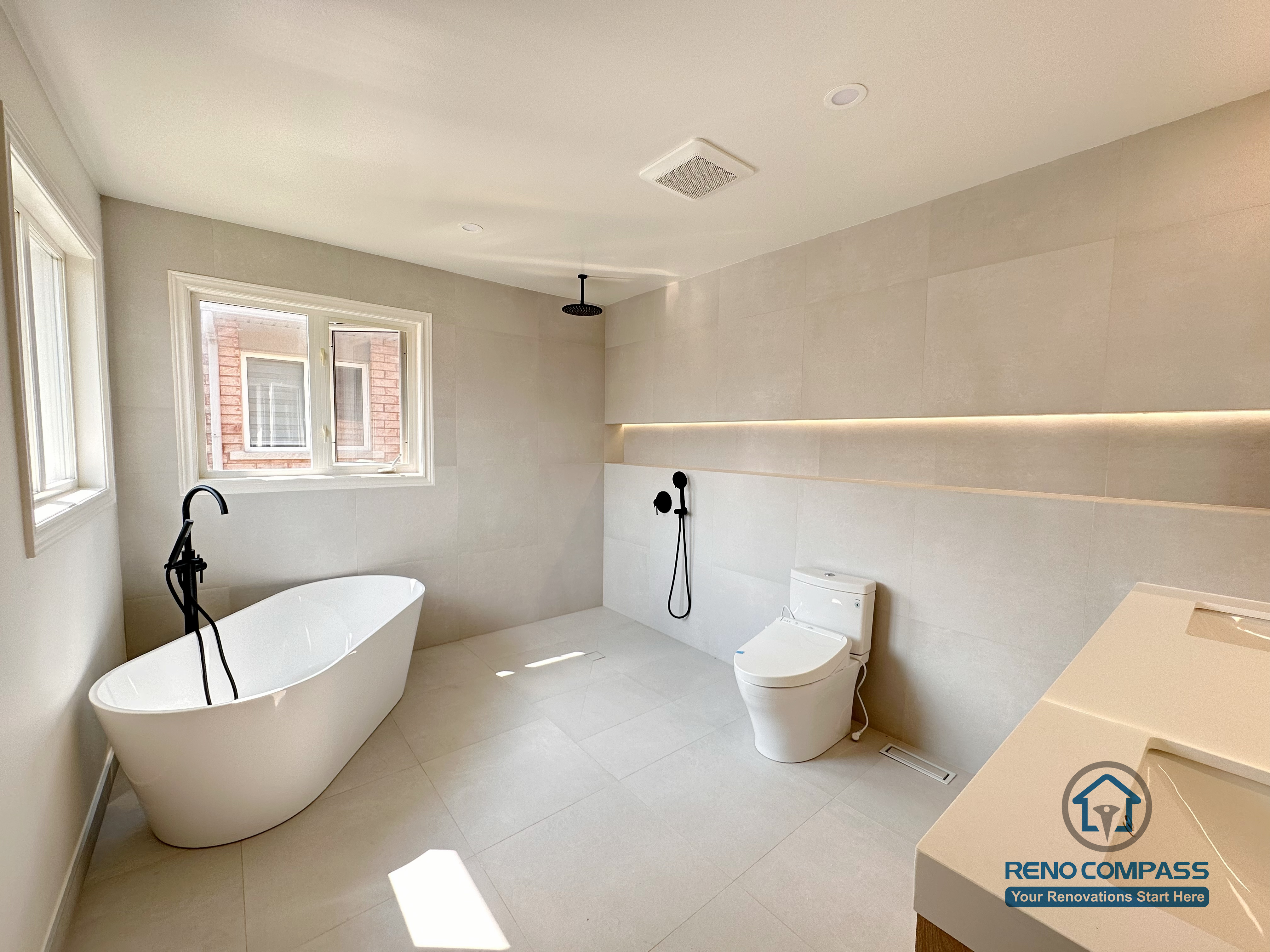 Modern bathroom renovation in Markham featuring a freestanding bathtub, walk-in shower, and wall-mounted matte black fixtures. Large-format tiles, soft natural light, and a minimalist layout create a calm, spa-like bathroom designed for comfort and everyday use.