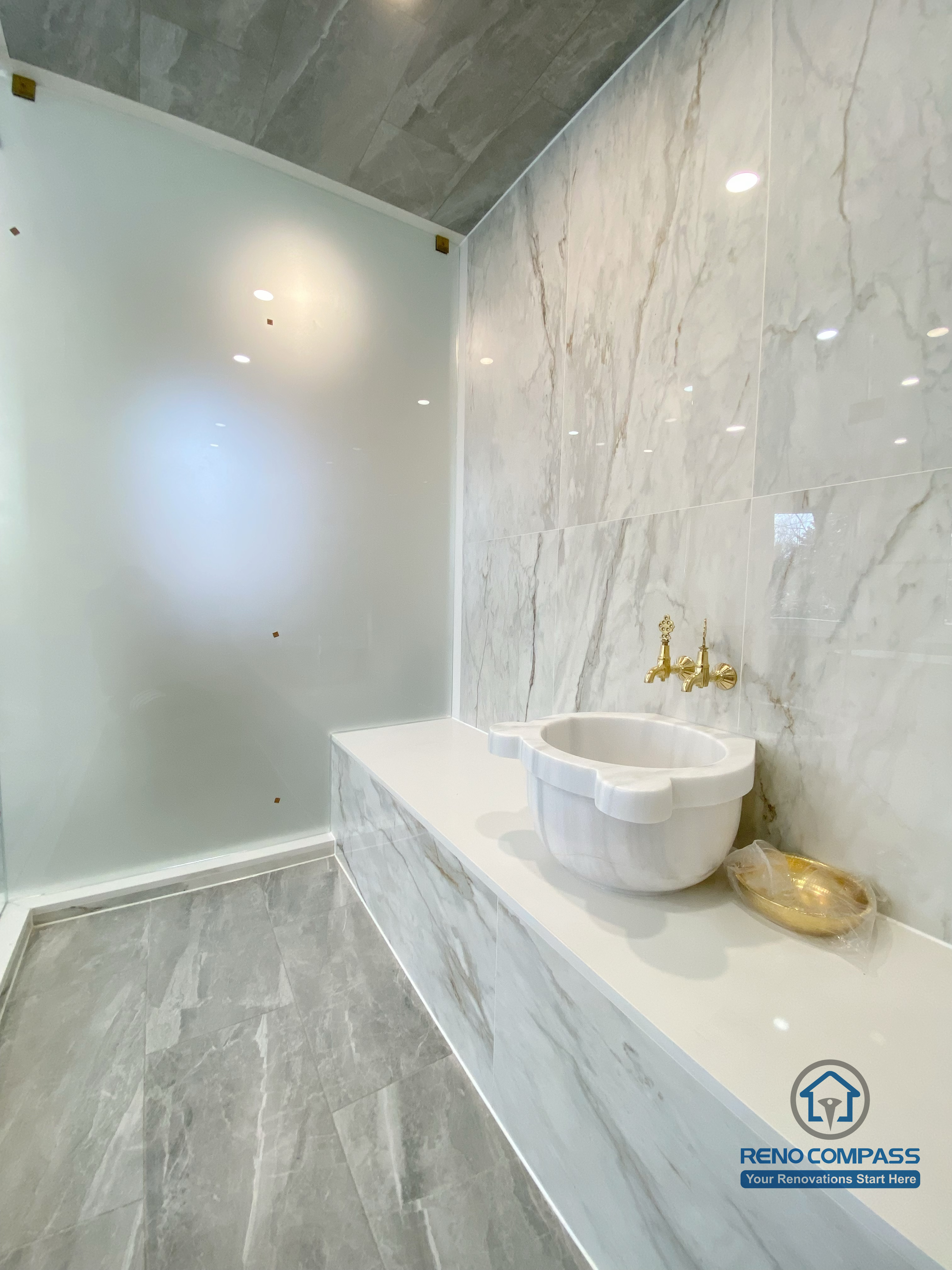 This Richmond Hill bathroom renovation showcases a bright and elegant design featuring a frameless glass shower enclosure, built-in bathtub, marble-style wall tiles, and gold-finish fixtures. The custom white vanity with integrated lighting mirror and large-format floor tiles enhance both functionality and visual openness. This project reflects high-quality craftsmanship and thoughtful layout planning for a modern bathroom renovation in Richmond Hill.