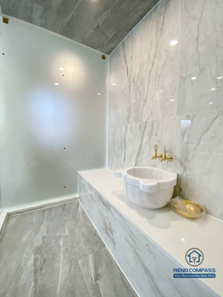 This Richmond Hill bathroom renovation showcases a bright and elegant design featuring a frameless glass shower enclosure, built-in bathtub, marble-style wall tiles, and gold-finish fixtures. The custom white vanity with integrated lighting mirror and large-format floor tiles enhance both functionality and visual openness. This project reflects high-quality craftsmanship and thoughtful layout planning for a modern bathroom renovation in Richmond Hill.