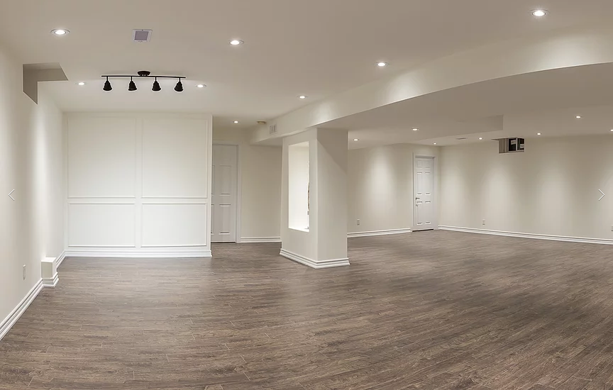 This open-concept finished basement from our Vaughan full house renovation features neutral walls, recessed lighting, and wood-look flooring. The design maximizes space and brightness, creating a versatile area perfect for family gatherings, entertainment, or a home office setup.