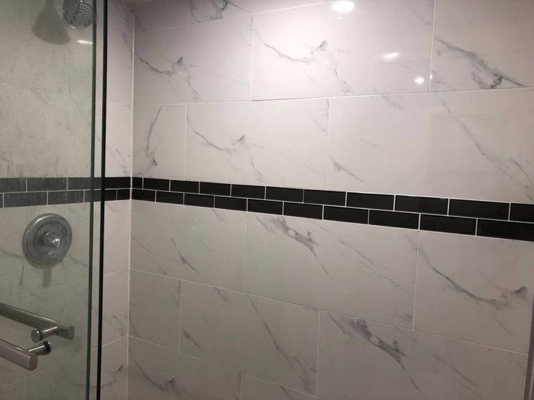 Custom shower installation as part of a Toronto basement renovation project, featuring marble-look porcelain wall tiles, black accent strip detailing, frameless glass enclosure, and modern chrome fixtures for a clean and contemporary finish.
