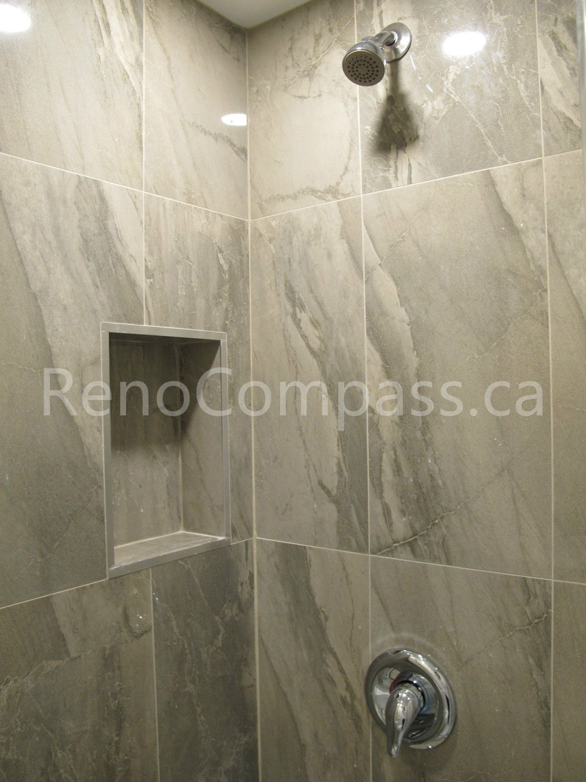 Close-up of custom shower tile installation in this Markham basement renovation, featuring marble-look porcelain tiles, recessed storage niche, and modern chrome fixtures. Completed by Reno Compass, this bathroom detail showcases precise tile work and functional design for a stylish and durable basement shower space.