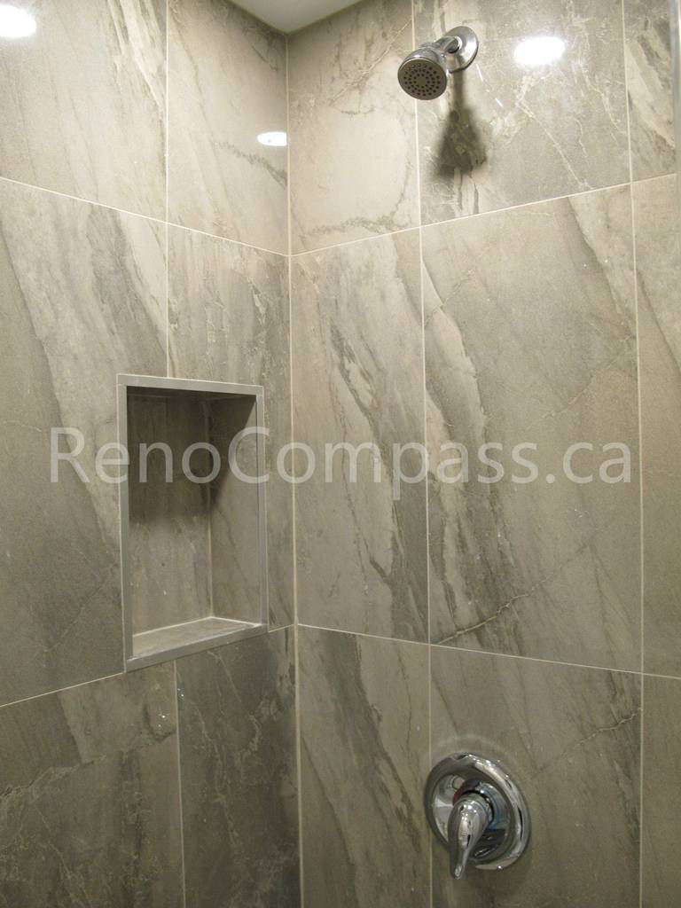 Close-up of custom shower tile installation in this Markham basement renovation, featuring marble-look porcelain tiles, recessed storage niche, and modern chrome fixtures. Completed by Reno Compass, this bathroom detail showcases precise tile work and functional design for a stylish and durable basement shower space.