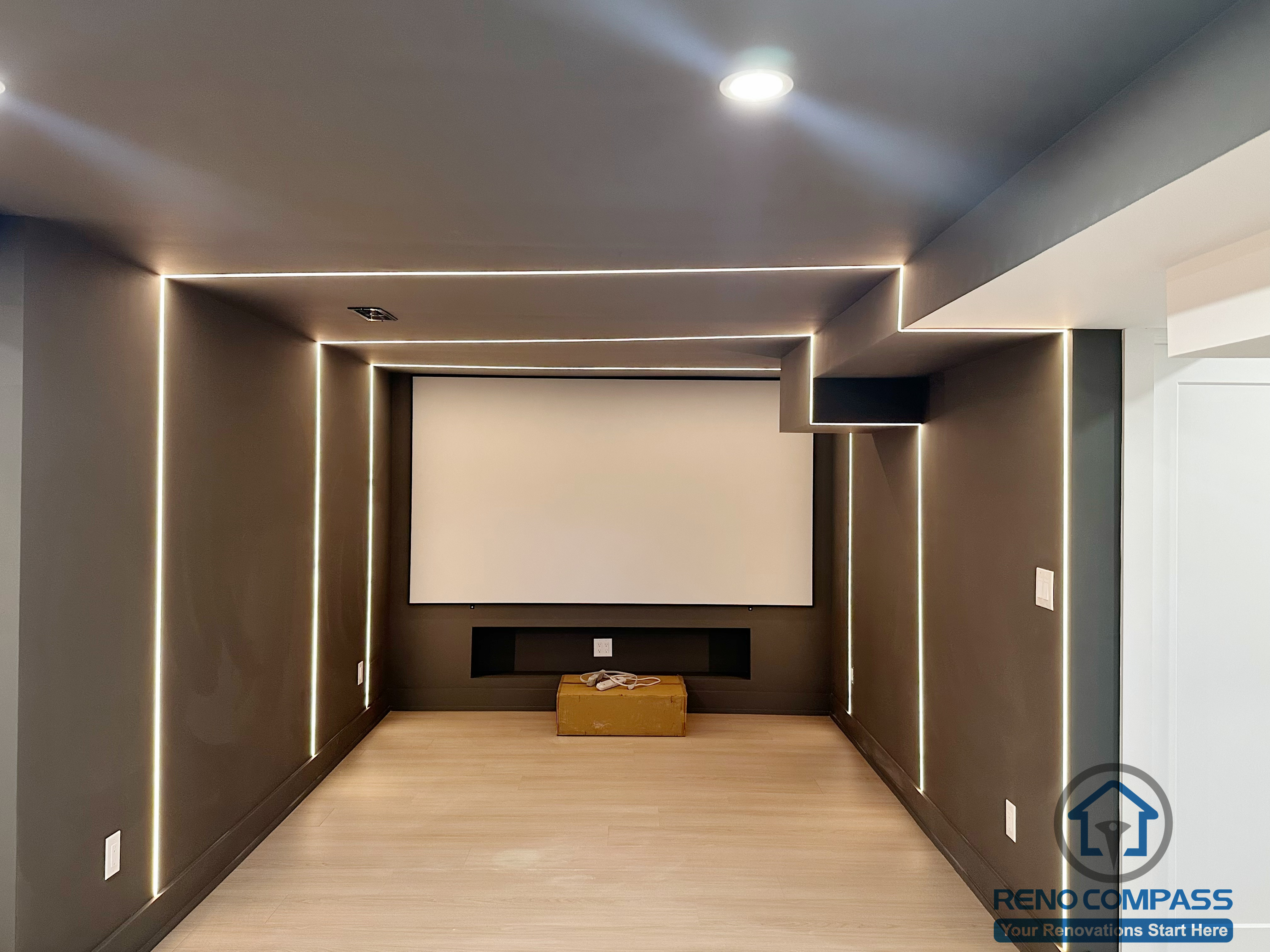 This Markham interior renovation features a dedicated home theater designed for an immersive and distraction-free viewing experience. Linear LED lighting is precisely integrated into the walls and ceiling to frame the space and guide visual focus toward the projection screen. Dark-toned finishes help control light reflection, enhancing screen clarity and overall ambiance. The compact, symmetrical layout prioritizes acoustics, comfort, and clean geometry, resulting in a modern media room that feels intentional, cinematic, and highly functional.
