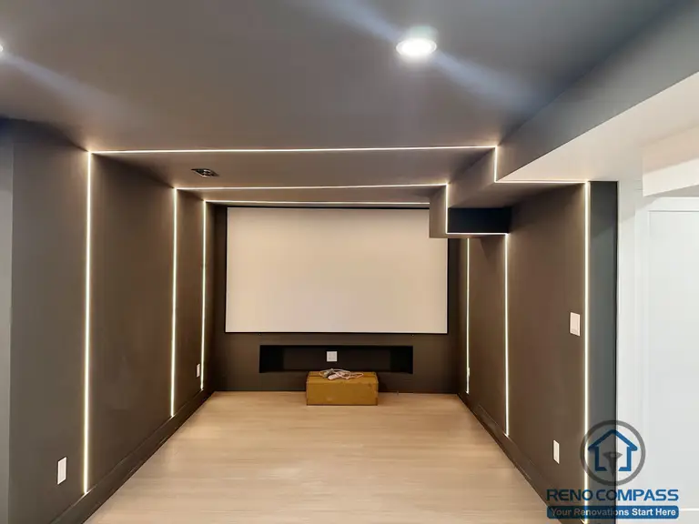 This Markham interior renovation features a dedicated home theater designed for an immersive and distraction-free viewing experience. Linear LED lighting is precisely integrated into the walls and ceiling to frame the space and guide visual focus toward the projection screen. Dark-toned finishes help control light reflection, enhancing screen clarity and overall ambiance. The compact, symmetrical layout prioritizes acoustics, comfort, and clean geometry, resulting in a modern media room that feels intentional, cinematic, and highly functional.
