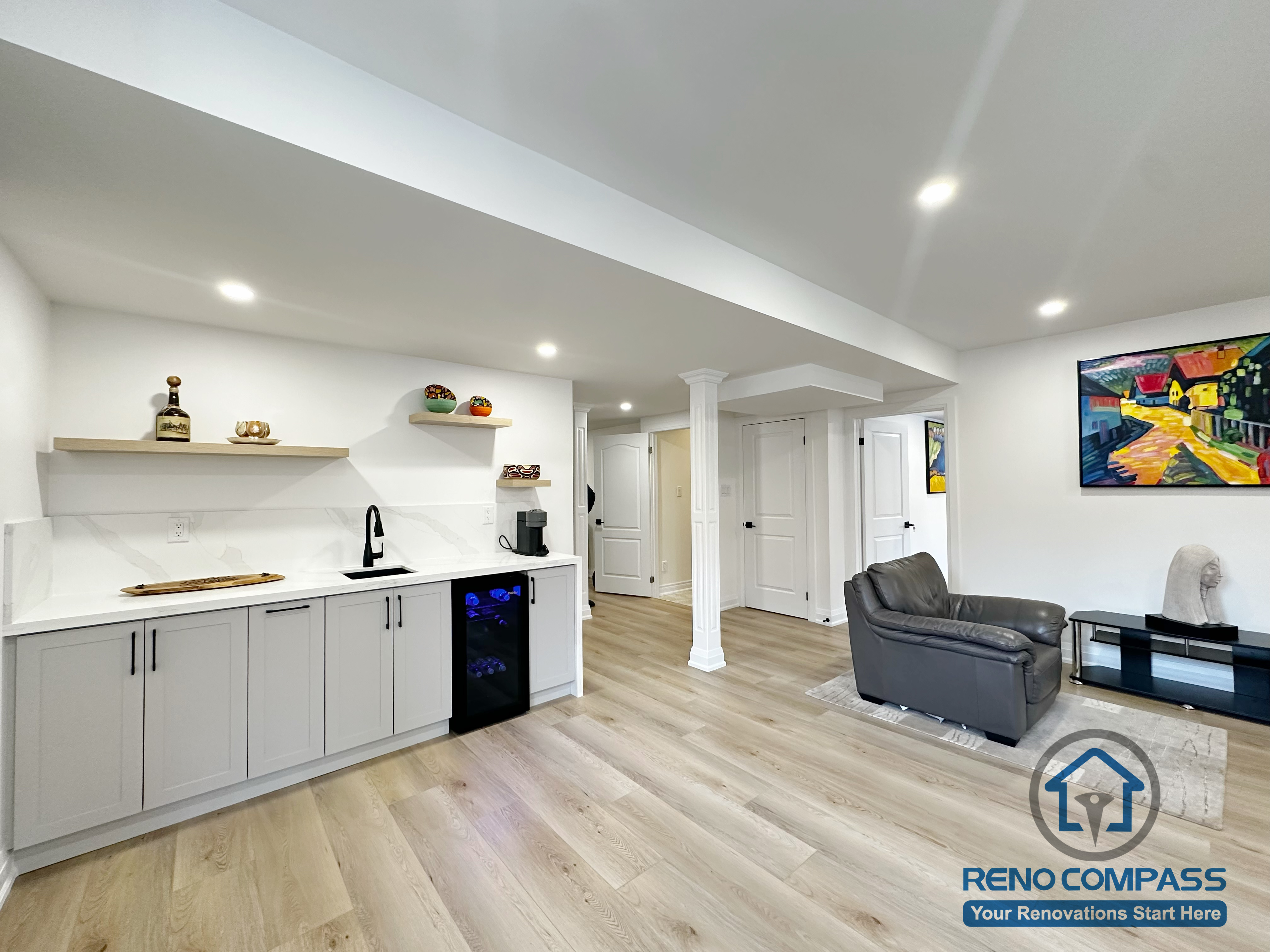 This Richmond Hill basement renovation features a custom wet bar seamlessly integrated into an open-concept lounge area. The design includes built-in cabinetry, open shelving, a compact beverage fridge, and a minimalist countertop for everyday use or entertaining. Wide-plank flooring, recessed lighting, and clean ceiling lines help create a bright, cohesive space. Structural columns were thoughtfully finished to blend into the layout, allowing the basement to function as a social hub, media area, or extended living space.