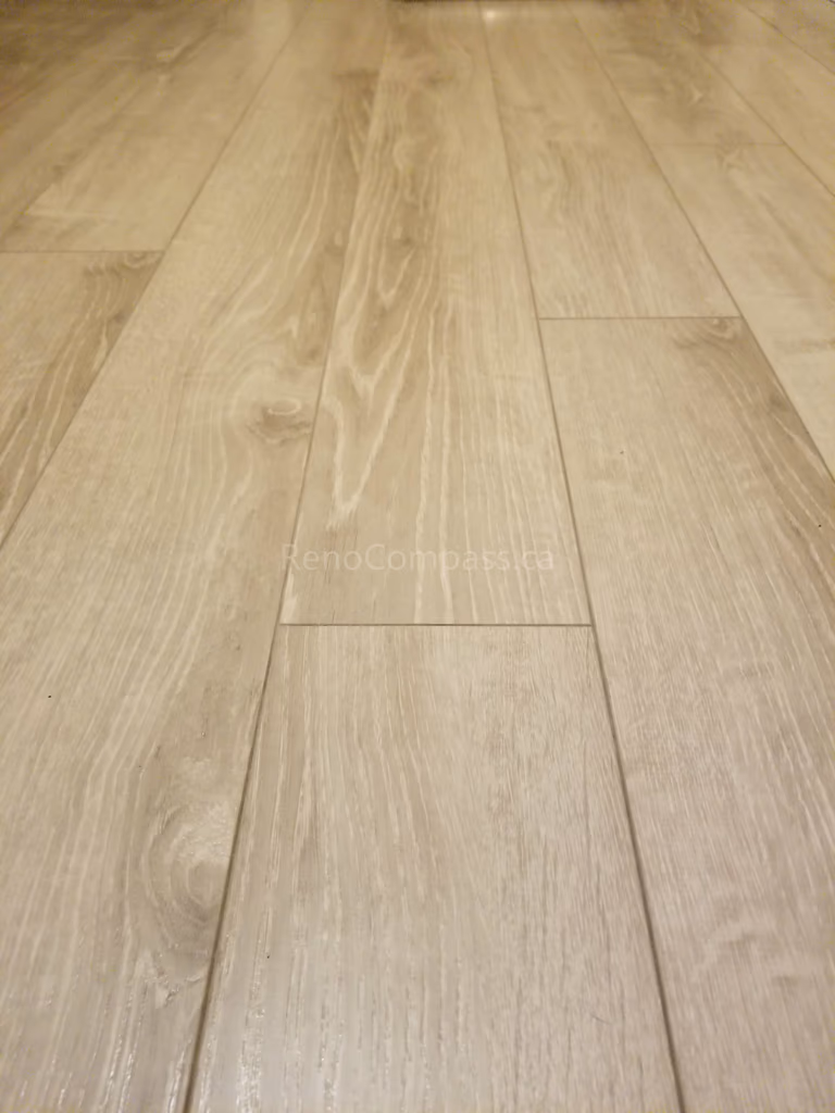 This Toronto basement renovation showcases newly installed light wood flooring paired with clean white baseboards for a modern and elegant finish. The durable laminate flooring enhances brightness and creates a warm, contemporary look while providing easy maintenance for basement living spaces. Installed by Reno Compass Inc., this flooring upgrade adds both style and functionality to the newly renovated basement interior.