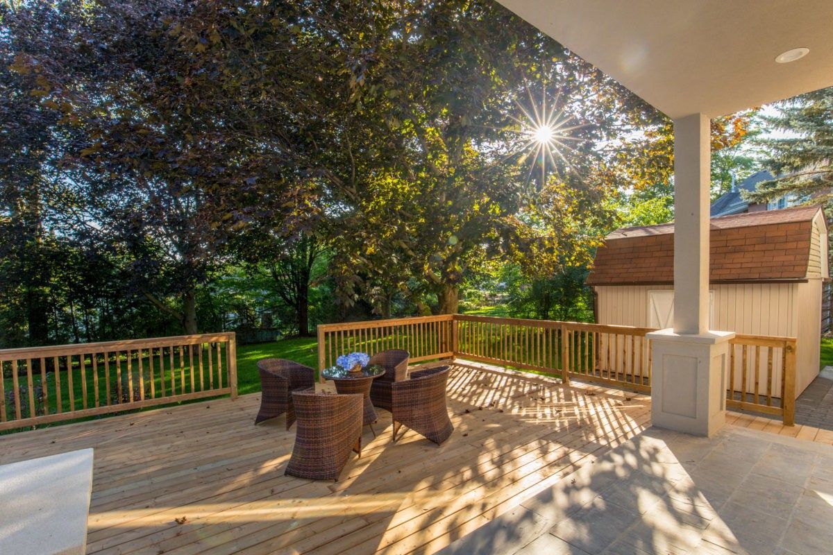 Beautifully renovated backyard deck of a 5000 sqft Toronto luxury home featuring a spacious wooden patio, covered outdoor seating area, and custom railing surrounded by mature trees and landscaped greenery. This outdoor living renovation creates a warm and inviting environment for relaxation and entertaining while seamlessly connecting indoor and outdoor spaces. Completed by Reno Compass Inc., a professional Toronto renovation company specializing in high-end residential renovations and custom outdoor living upgrades.