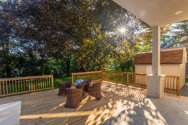 Beautifully renovated backyard deck of a 5000 sqft Toronto luxury home featuring a spacious wooden patio, covered outdoor seating area, and custom railing surrounded by mature trees and landscaped greenery. This outdoor living renovation creates a warm and inviting environment for relaxation and entertaining while seamlessly connecting indoor and outdoor spaces. Completed by Reno Compass Inc., a professional Toronto renovation company specializing in high-end residential renovations and custom outdoor living upgrades.